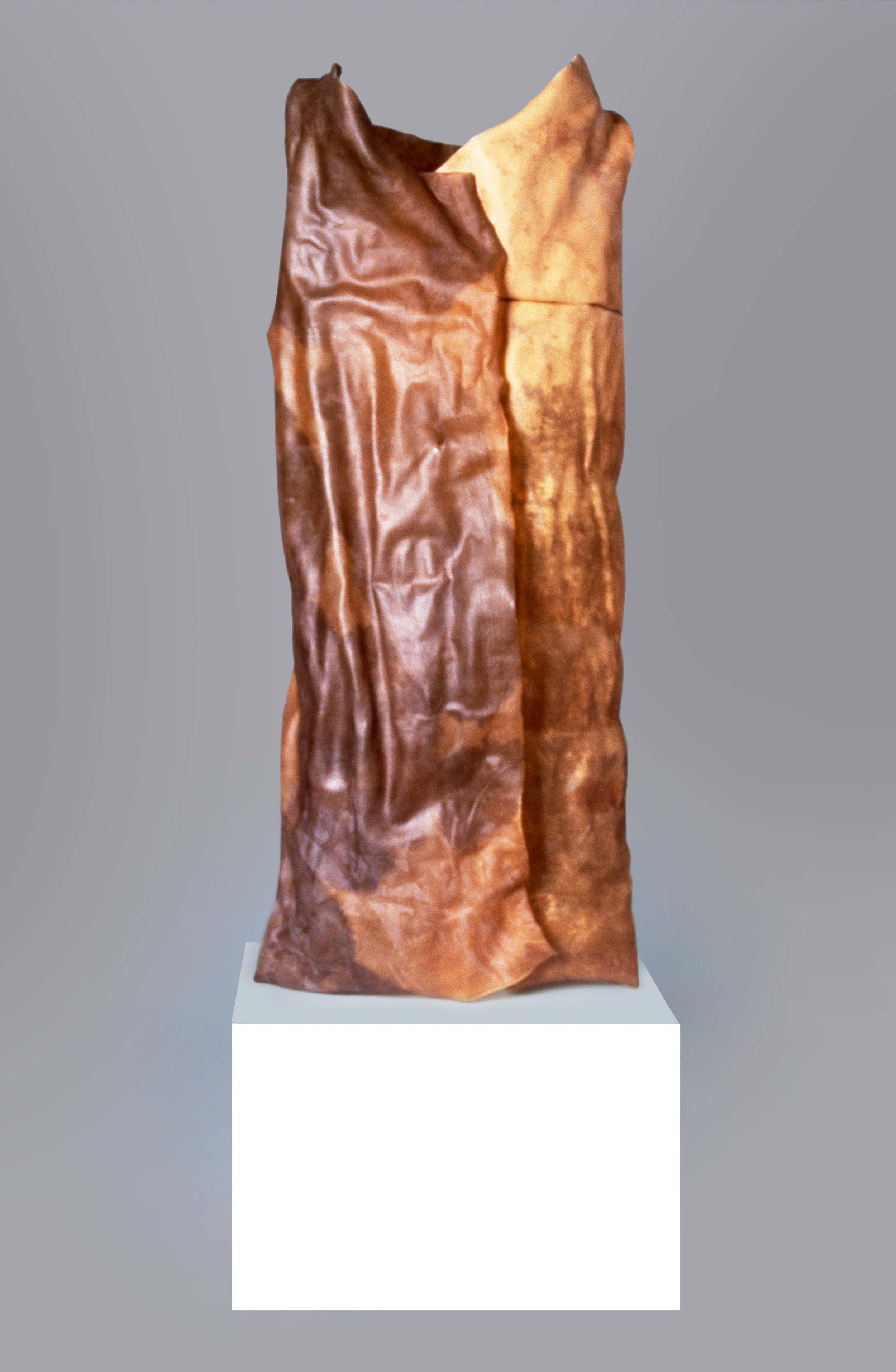 A tall, abstract sculpture made of textured, reddish-brown material, displayed on a white pedestal against a gray background.