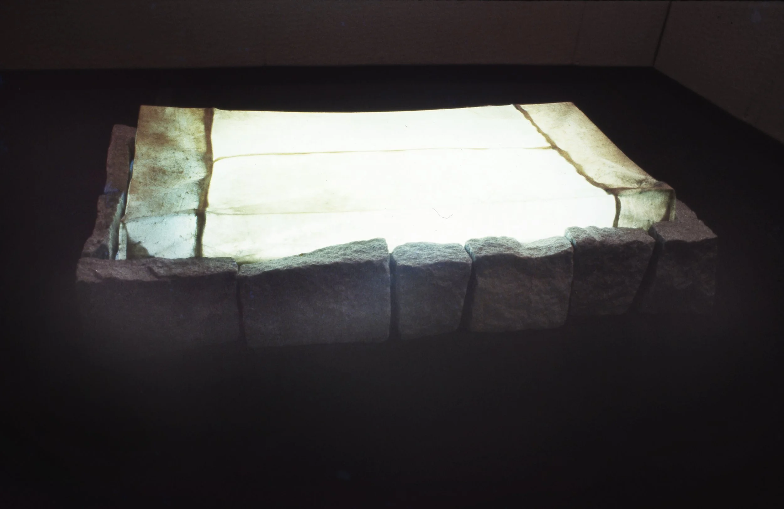 A rectangular stone fire pit or fireplace with light-colored stones inside.