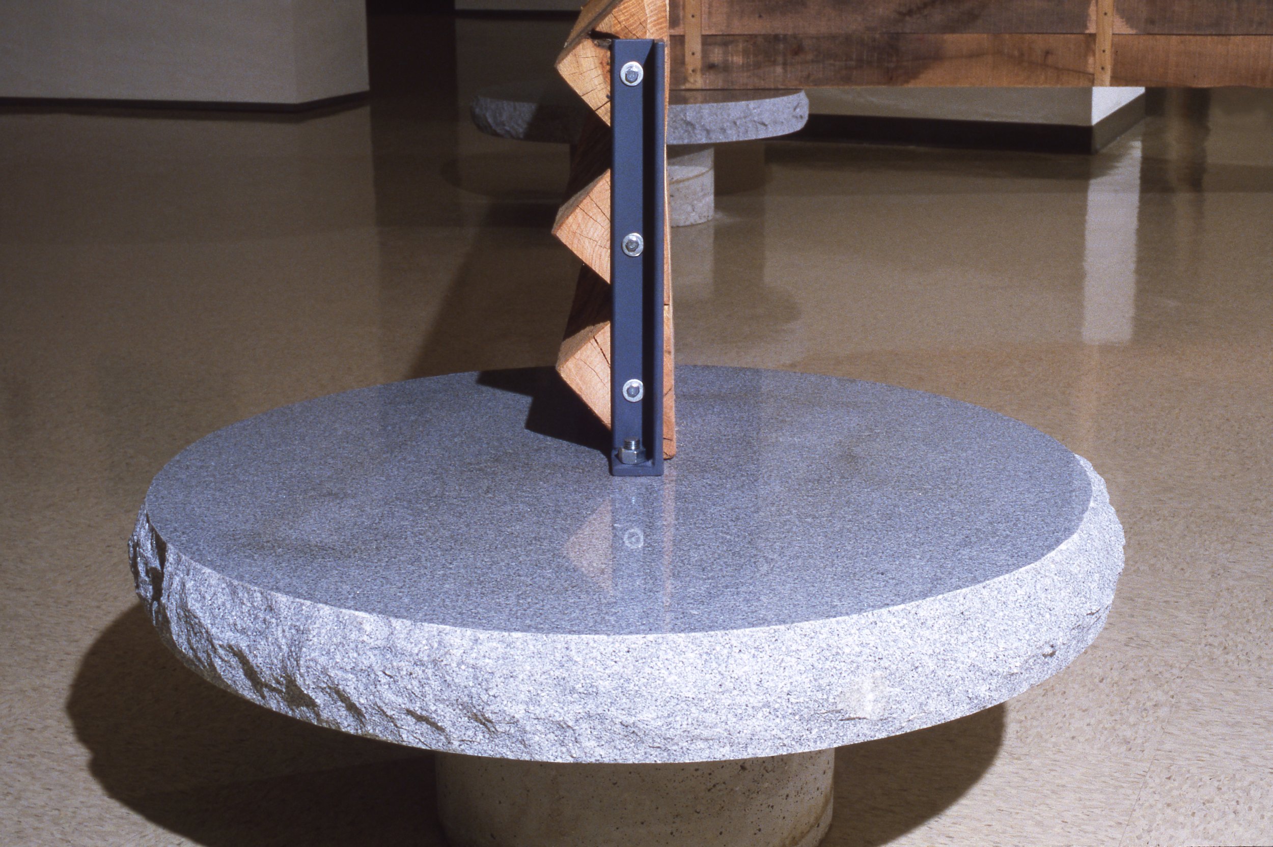Close-up of a large, round granite stone with a black metal ruler standing vertically on top, attached with screws, in an indoor setting.