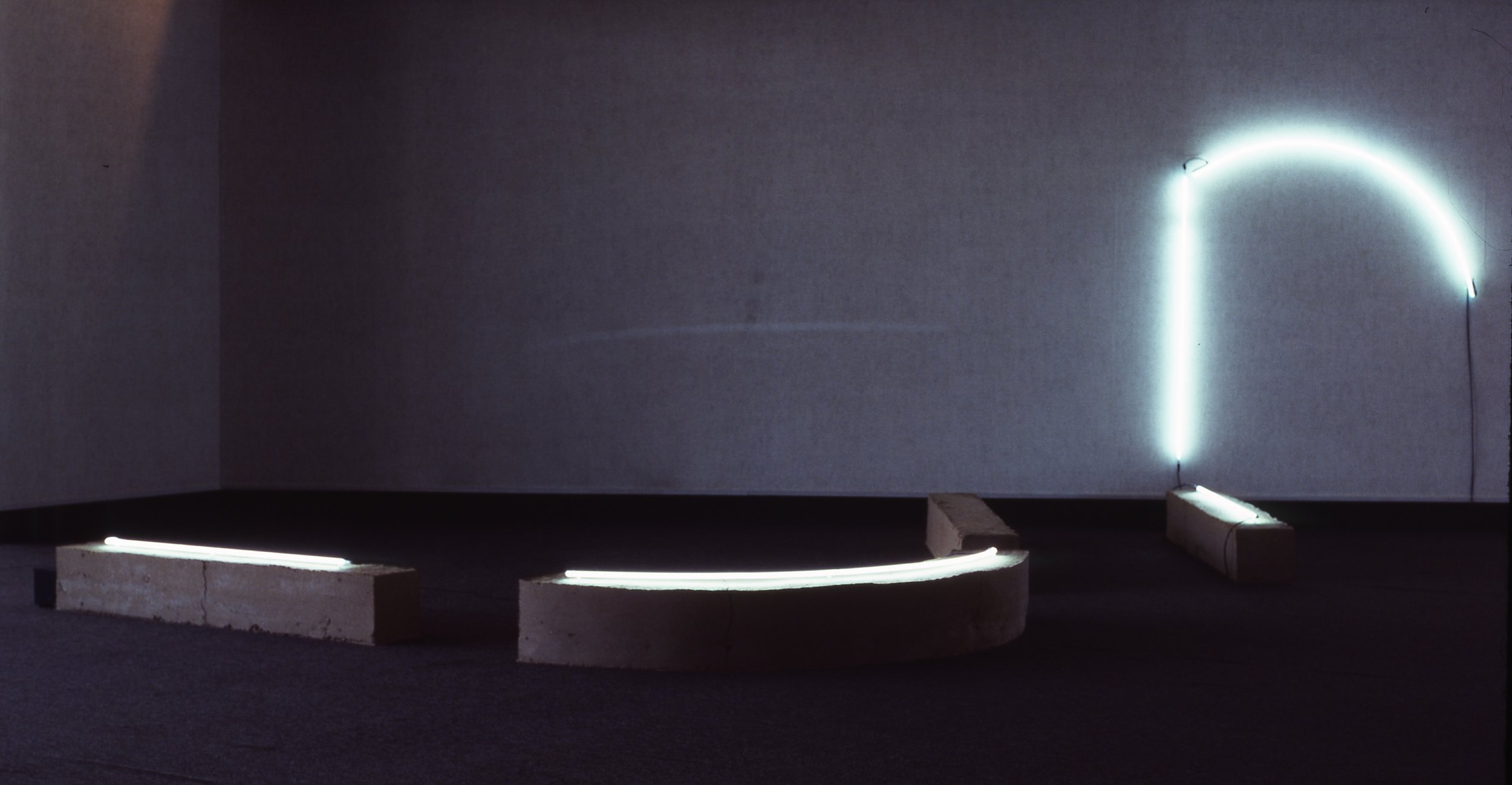 Minimalist art installation with concrete blocks and LED light strips on a dark wall.