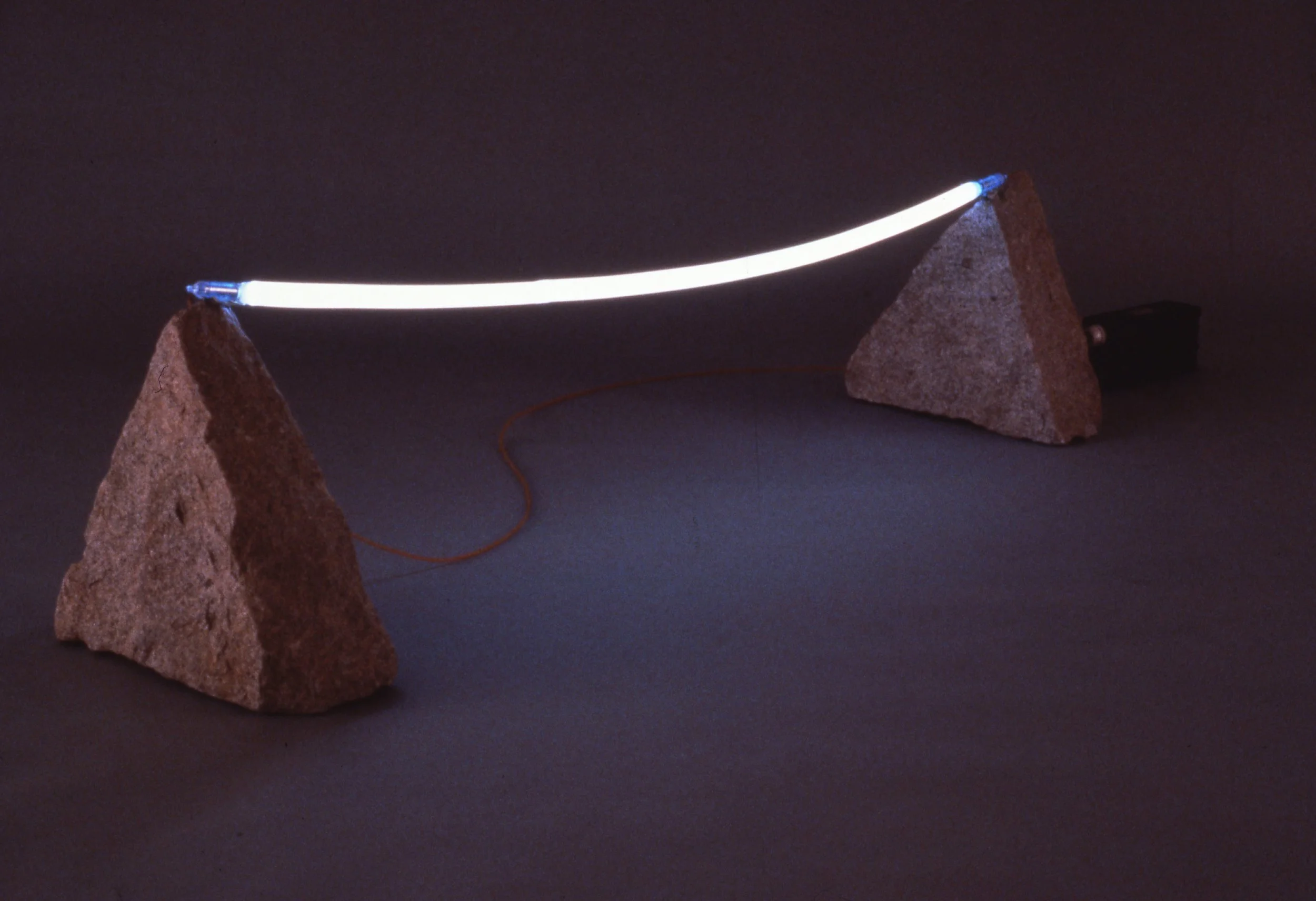 A glowing light fixture stretched between two large rocks on a dark surface.