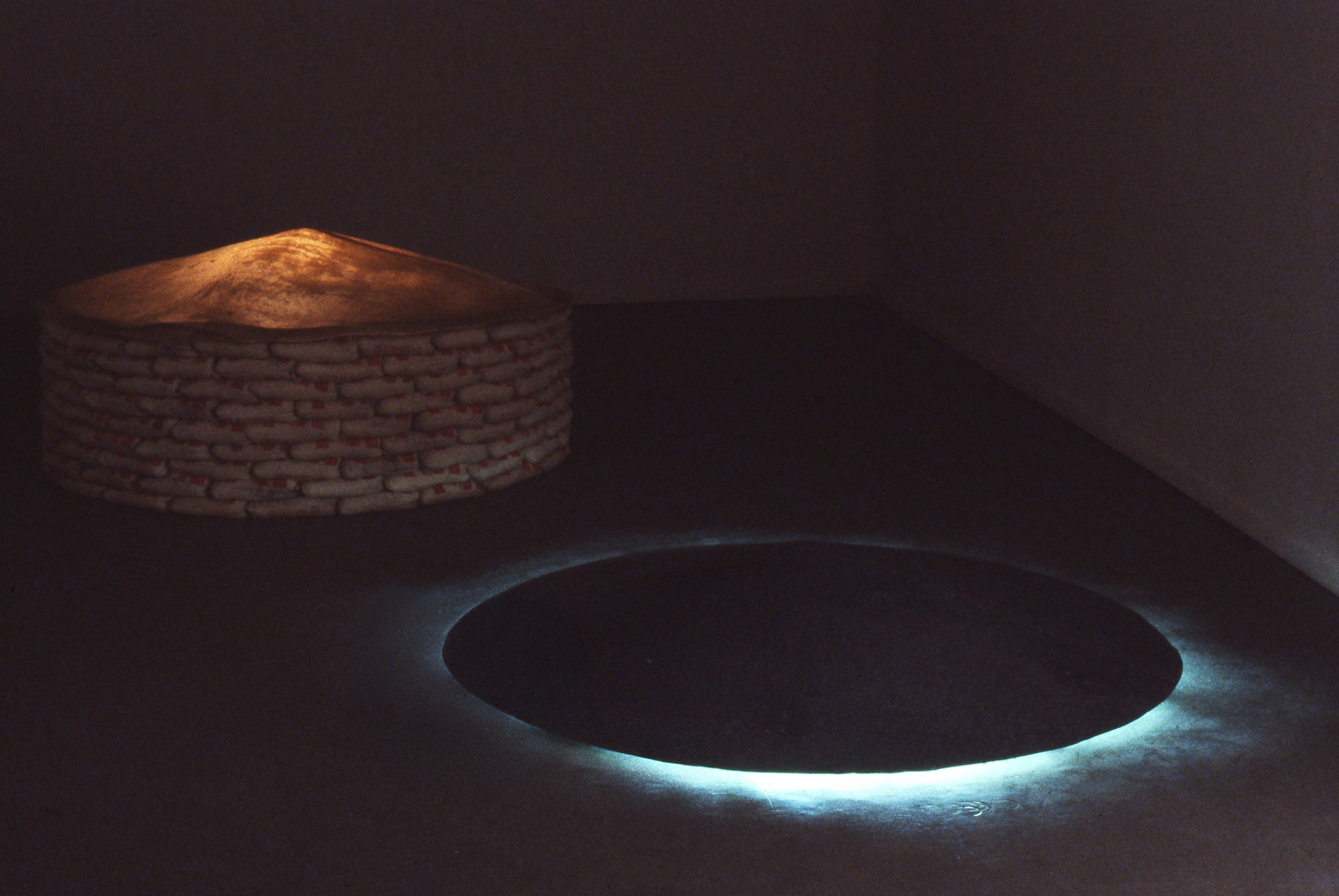 A circular brick stovetop with a black oval opening in the center, surrounded by a blue glow, in a dark room.