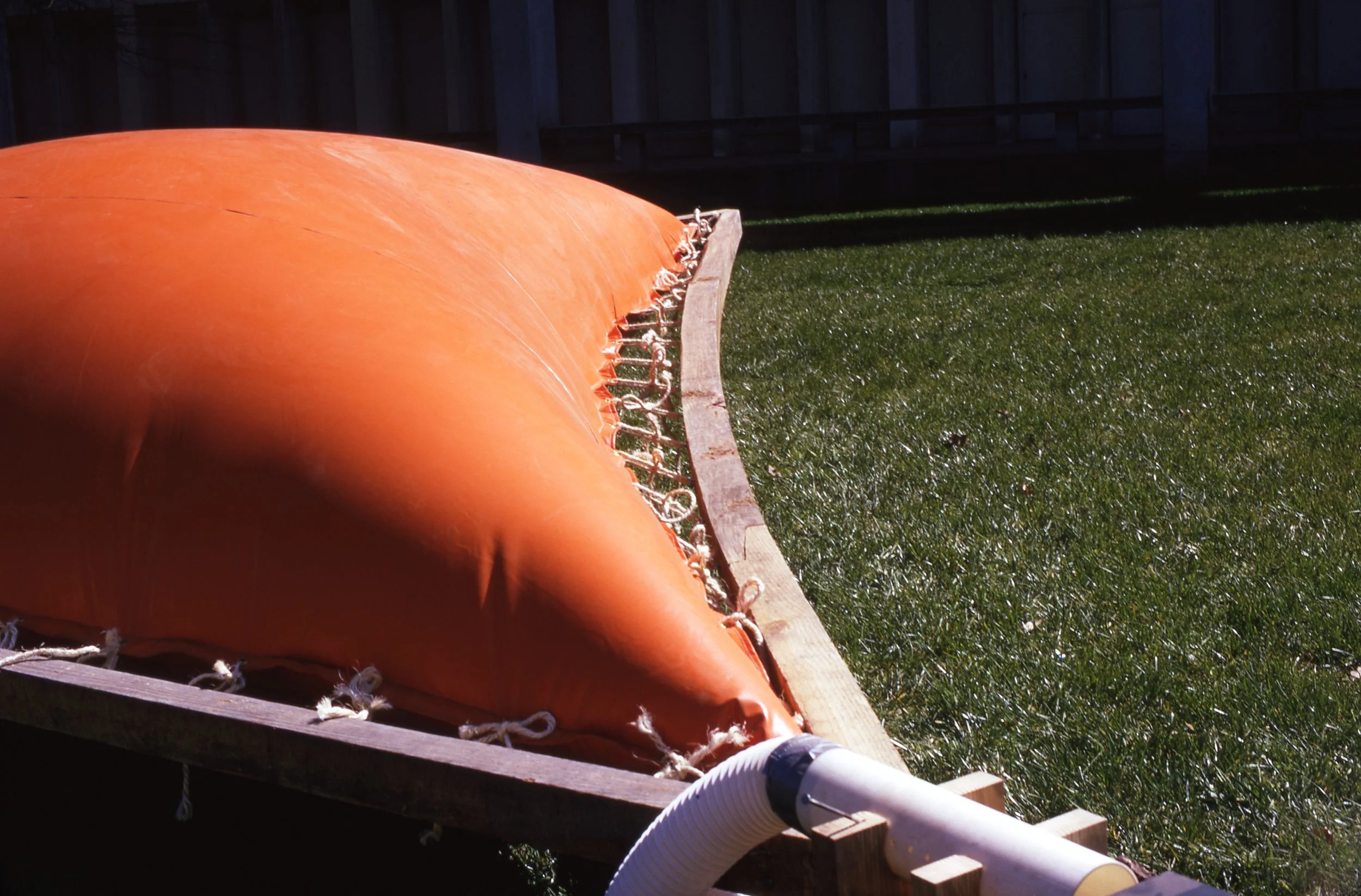 Close-up of an orange inflatable water slide on a grassy backyard with a wooden fence in the background.