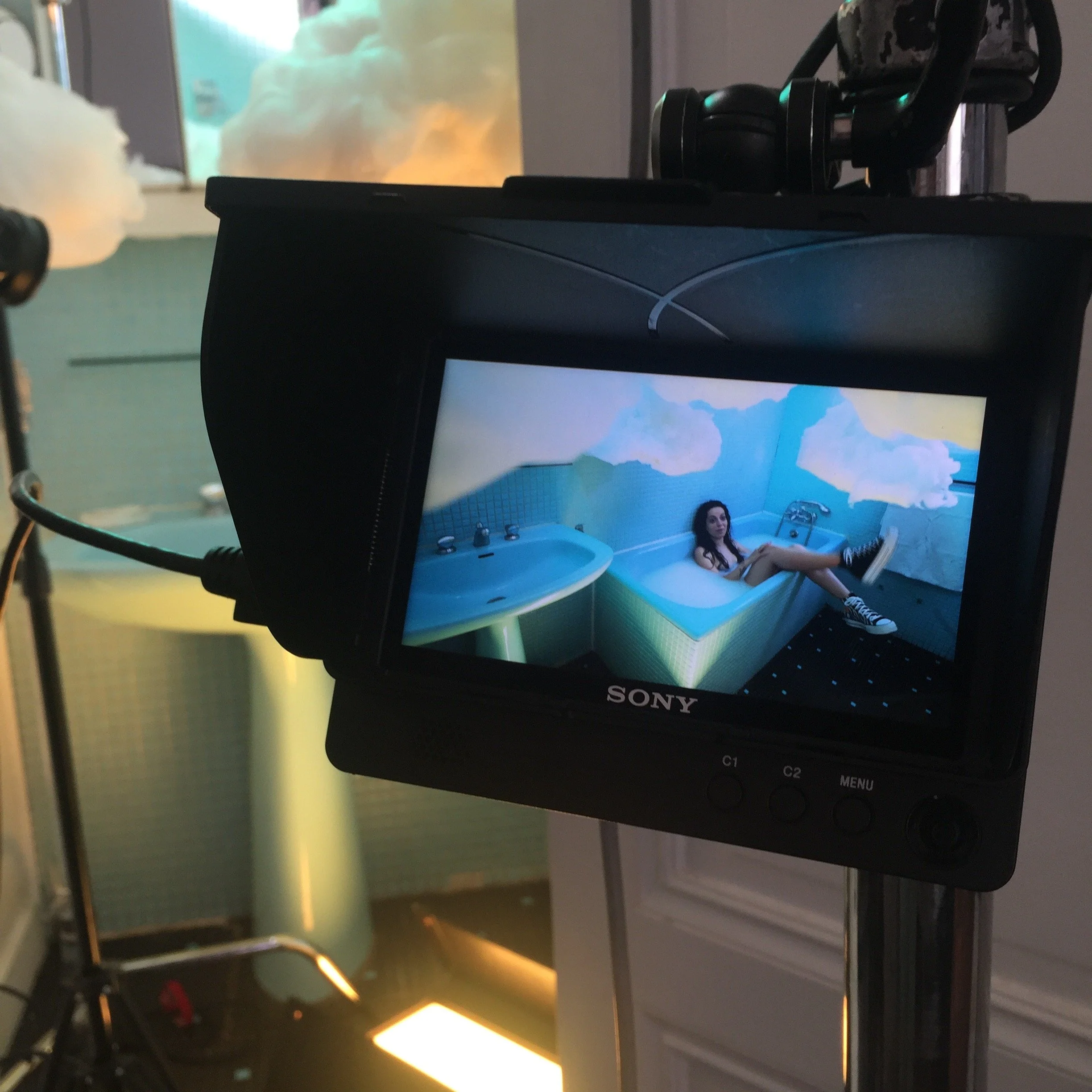 Un écran de caméra montrant une femme assise dans une baignoire dans une pièce décorée avec des nuages sur les murs.