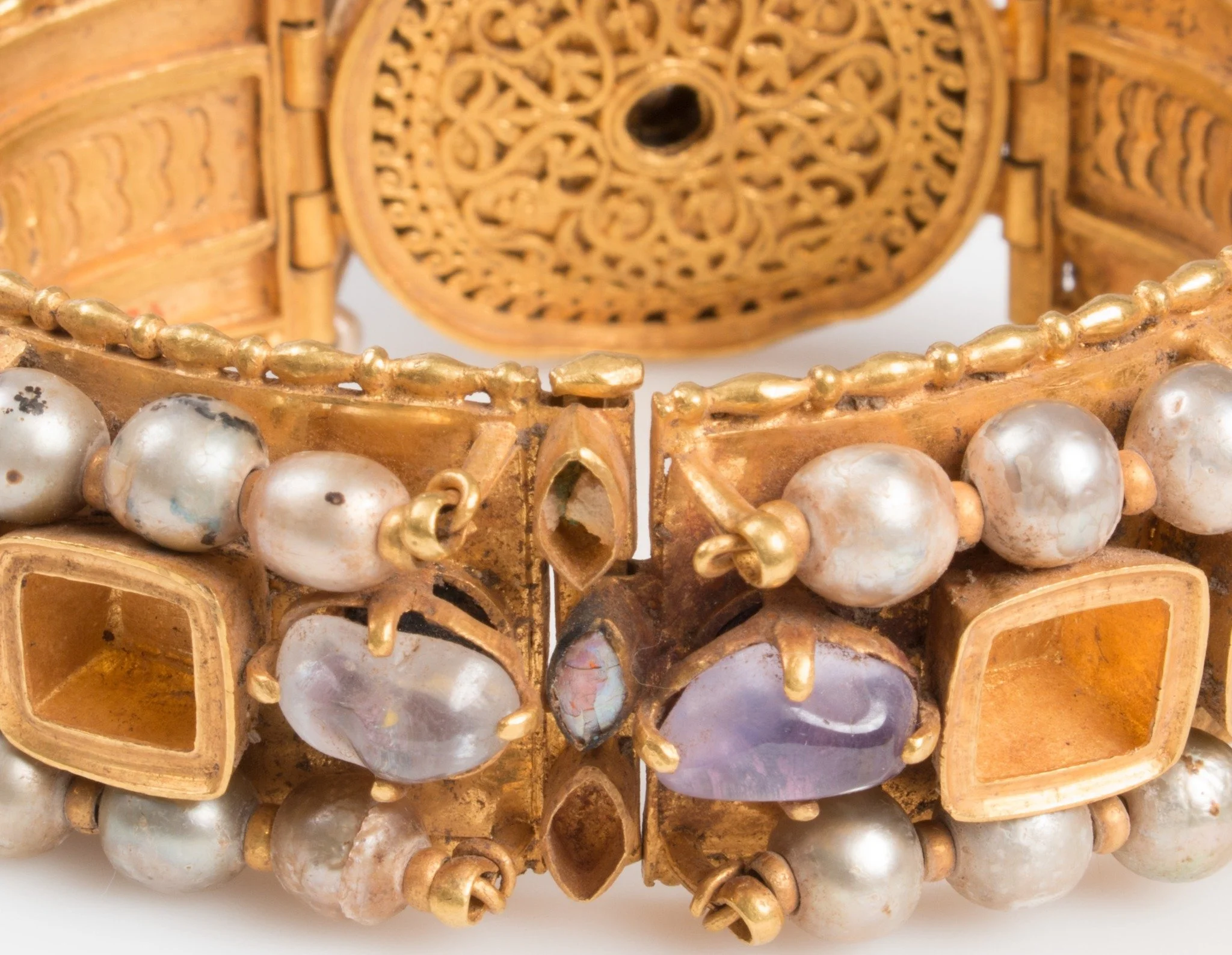 Close-up of an ornate, vintage gold bracelet adorned with white pearls, purple semi-precious stones, and gold beads.