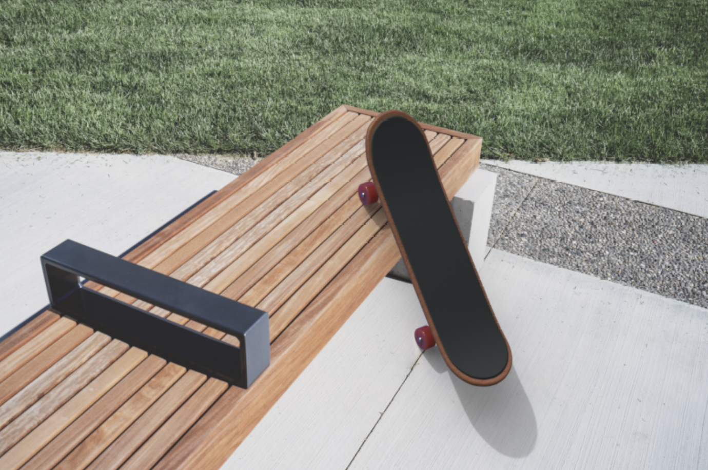 Skateboard leaning against a wooden bench outdoors on concrete pavement, with grass in the background.
