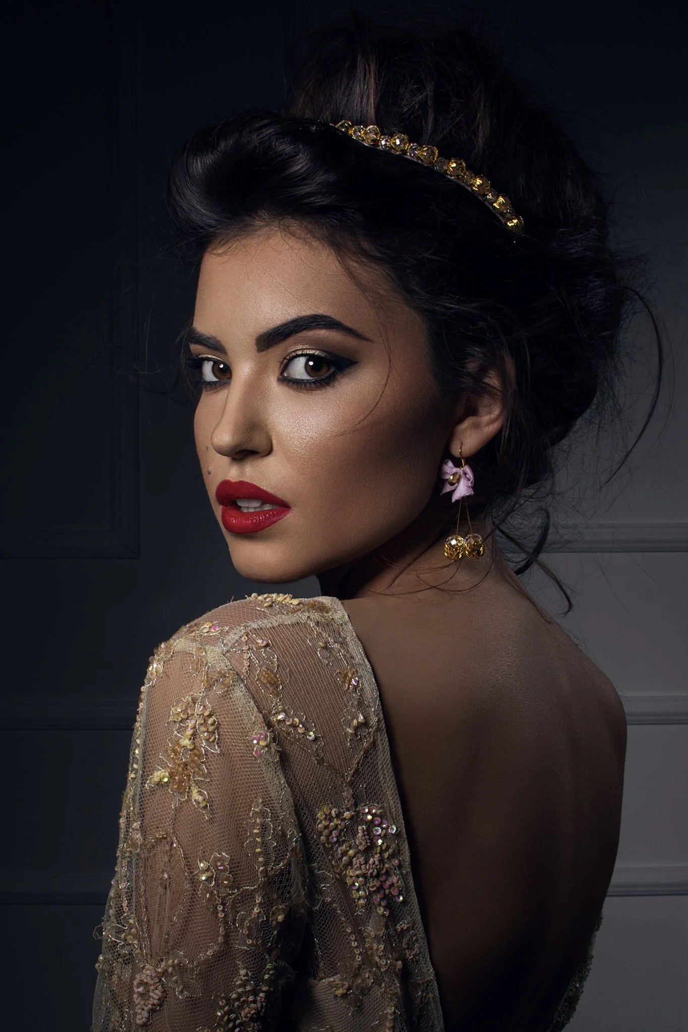 Woman with red lips, bold make up, gold lace backless dress, statement earrings and gold jewelled hairband