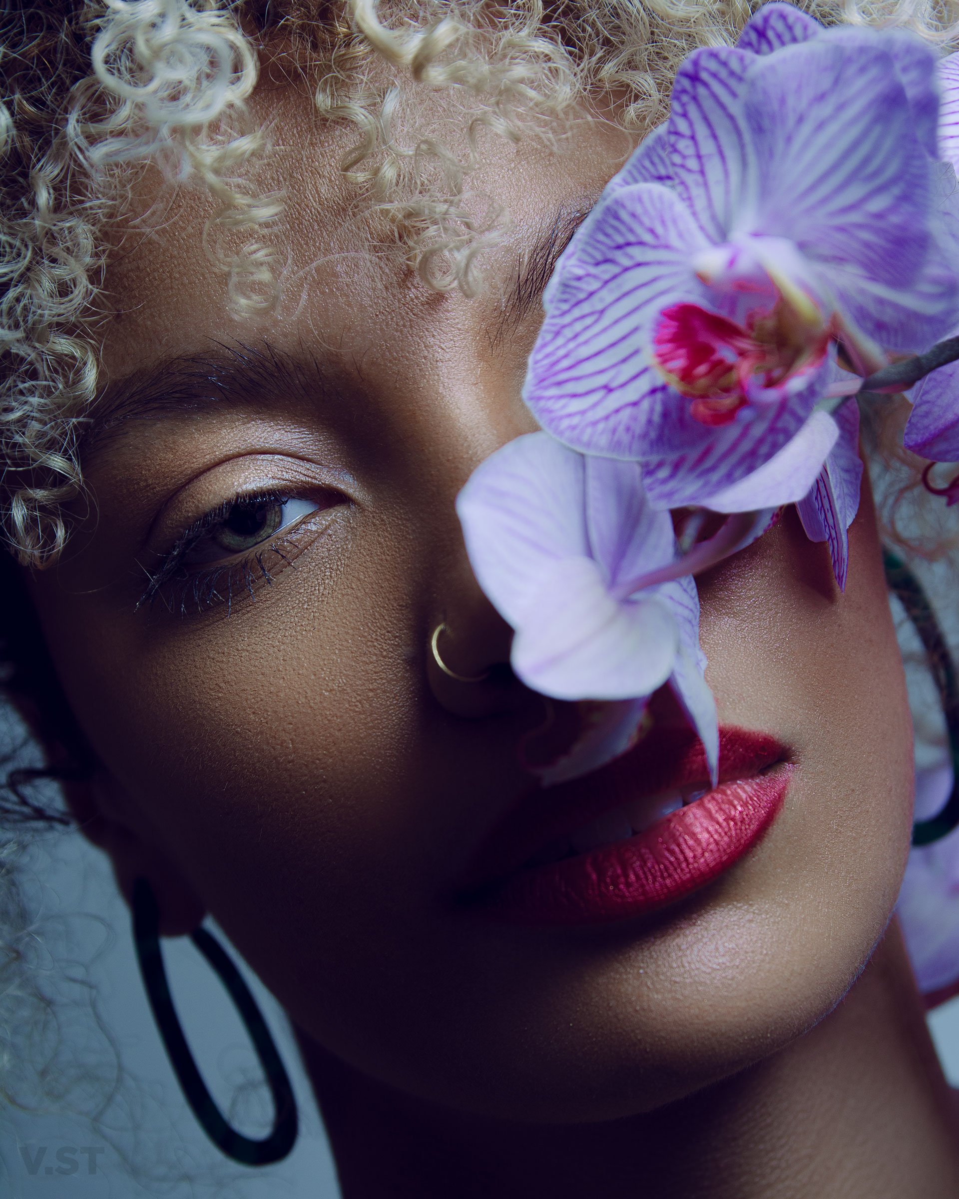 Curly hair woman with nose ring and earrings posing with flower