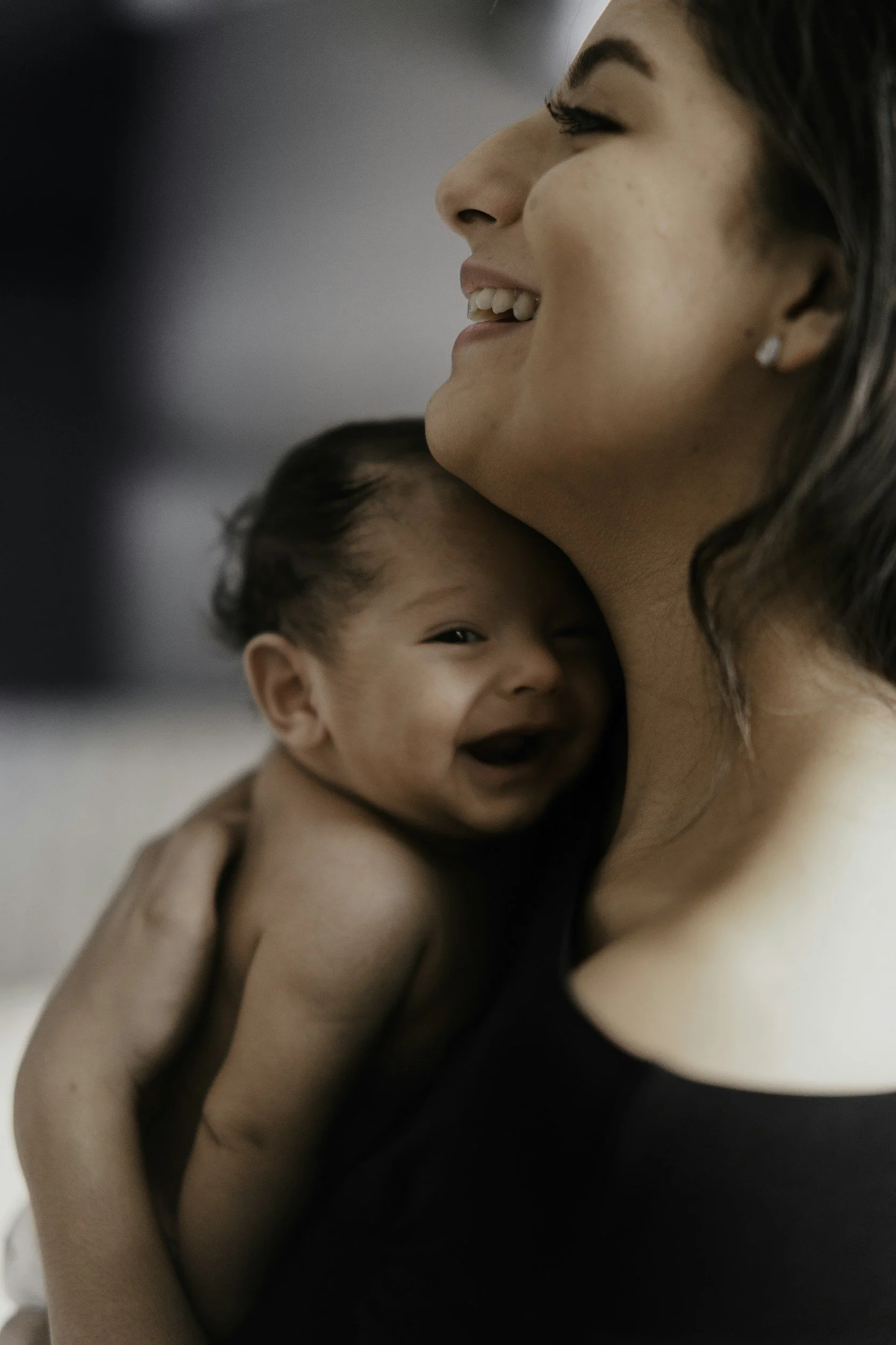 Une femme souriante tient un bébé contre elle, dans un cadre intime et chaleureux.