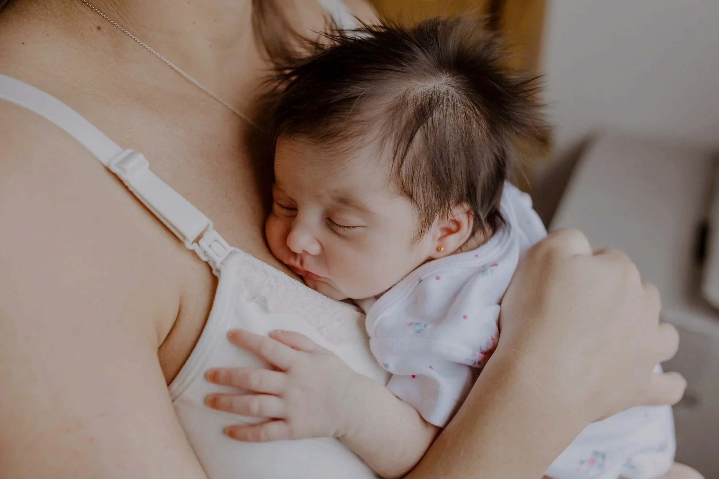 Une mère tient son bébé contre elle, le bébé dort paisiblement avec la tête appuyée contre sa poitrine.