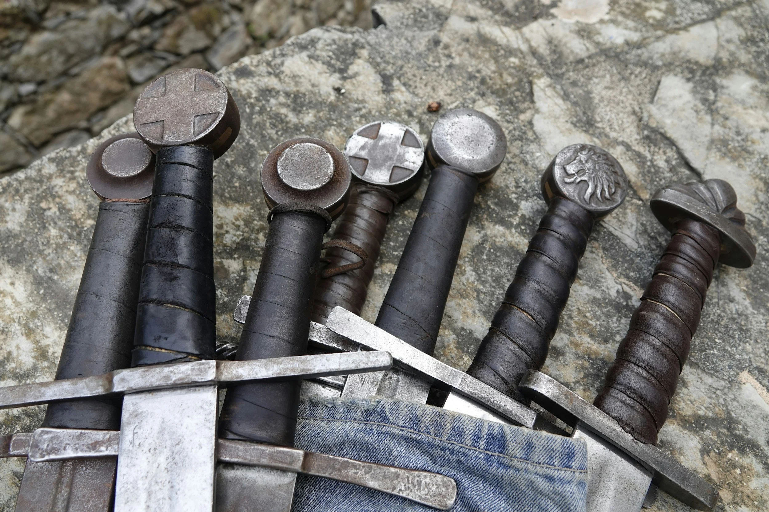A collection of eight vintage swords with various shaped hilts, laid out on a rough stone surface.