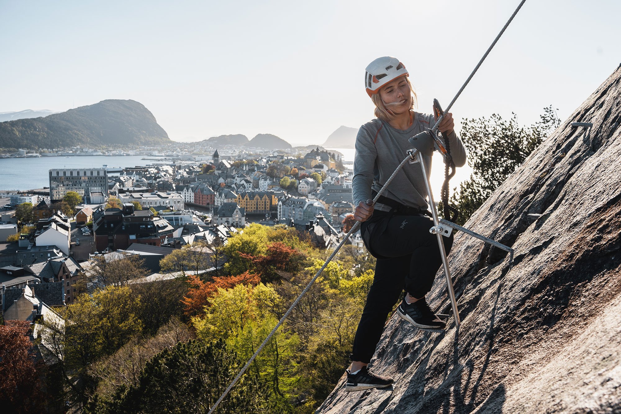 Woman rock climbing on a steep cliff with a city and water in the background