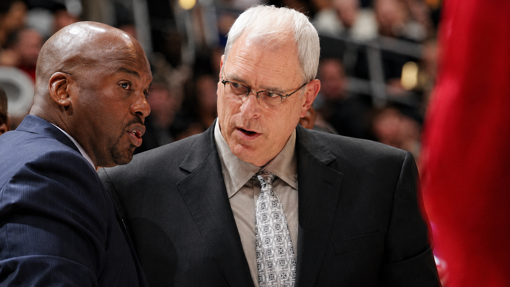 Coach Phil Jackson and Chuck Person having a conversation, with a blurred audience in the background.