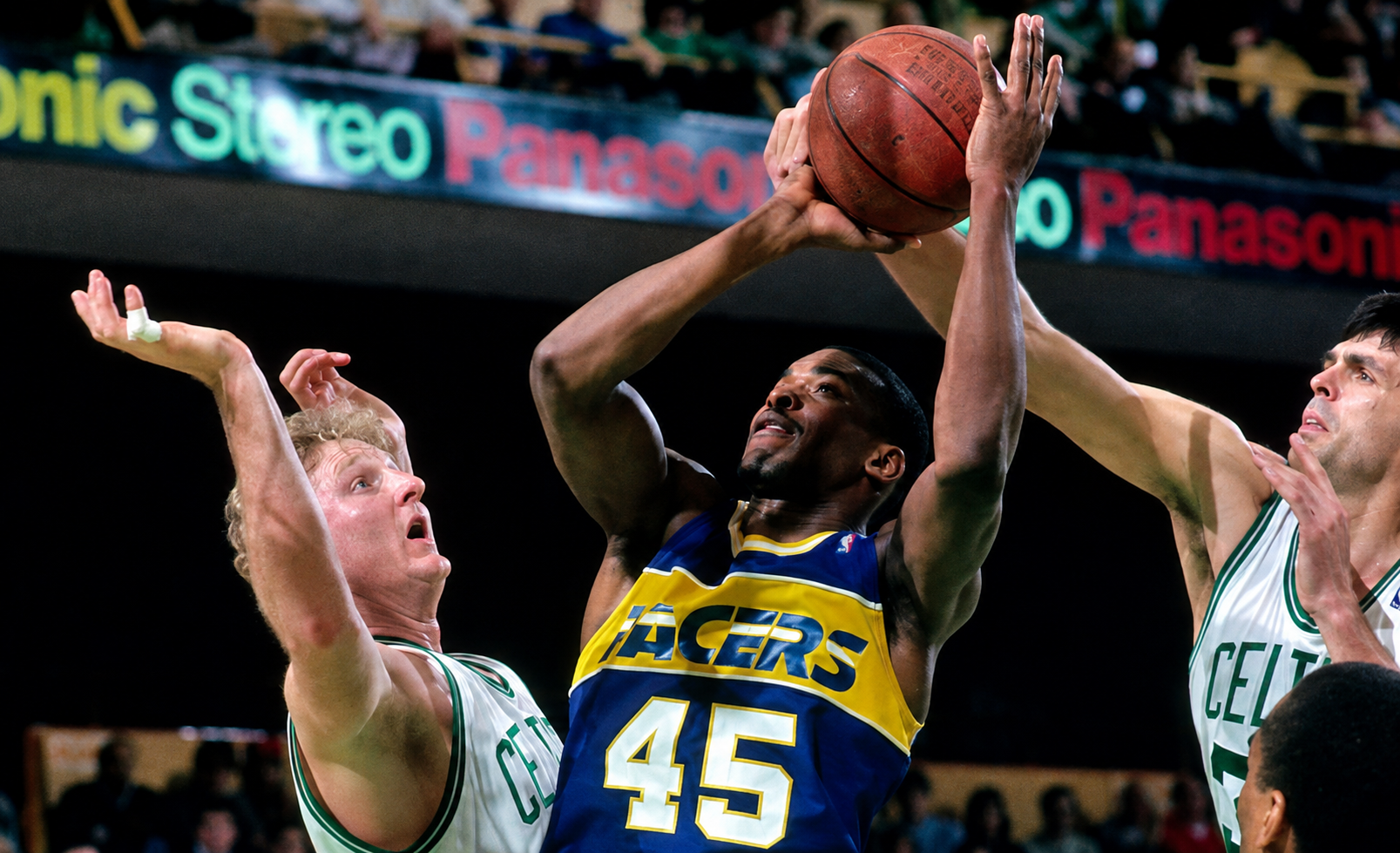 A basketball player from the Lakers jumping to make a shot, guarded by players from the Celtics during a game.