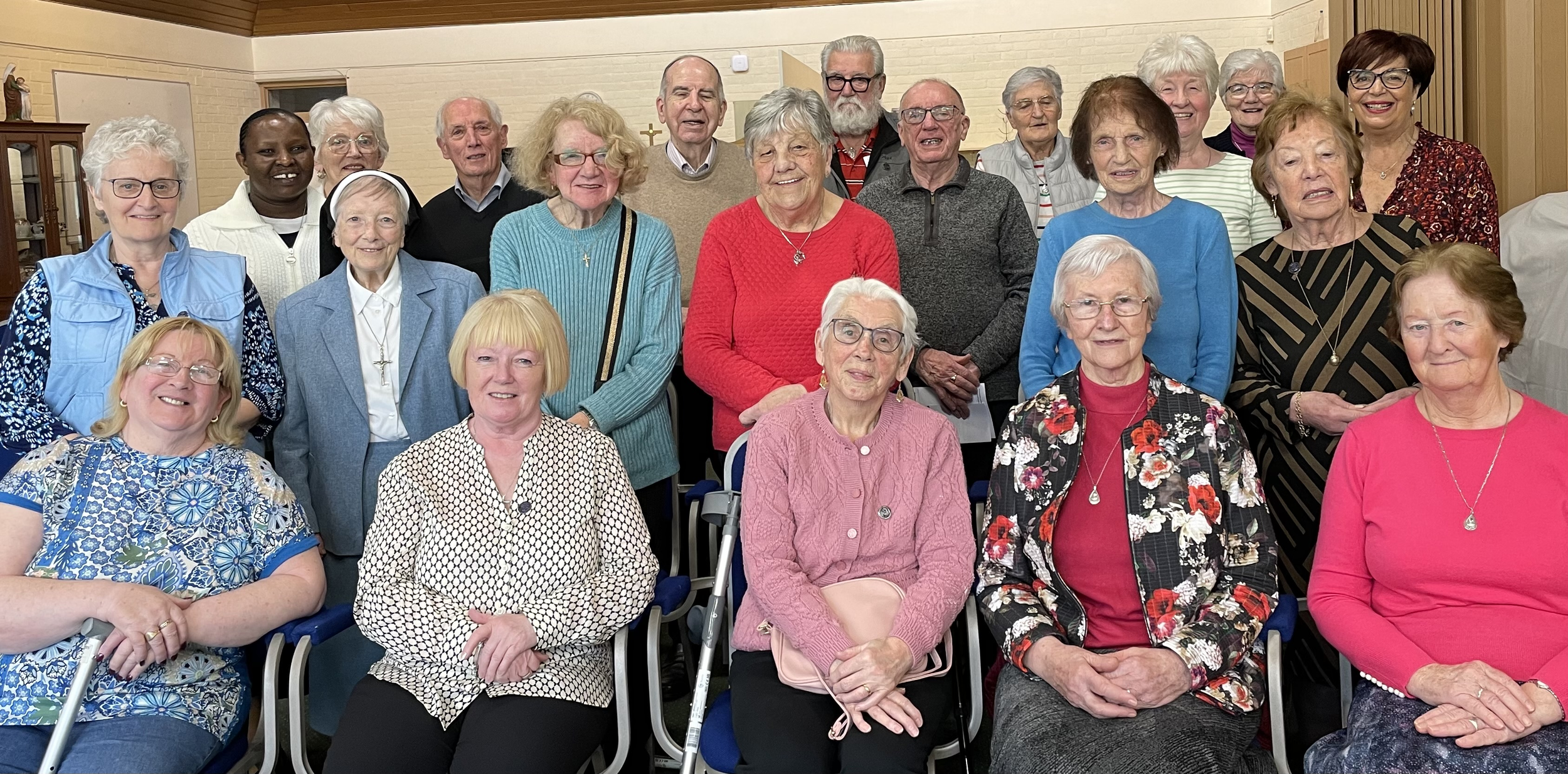 Group of elderly women and men posing together indoors in a community or social setting.