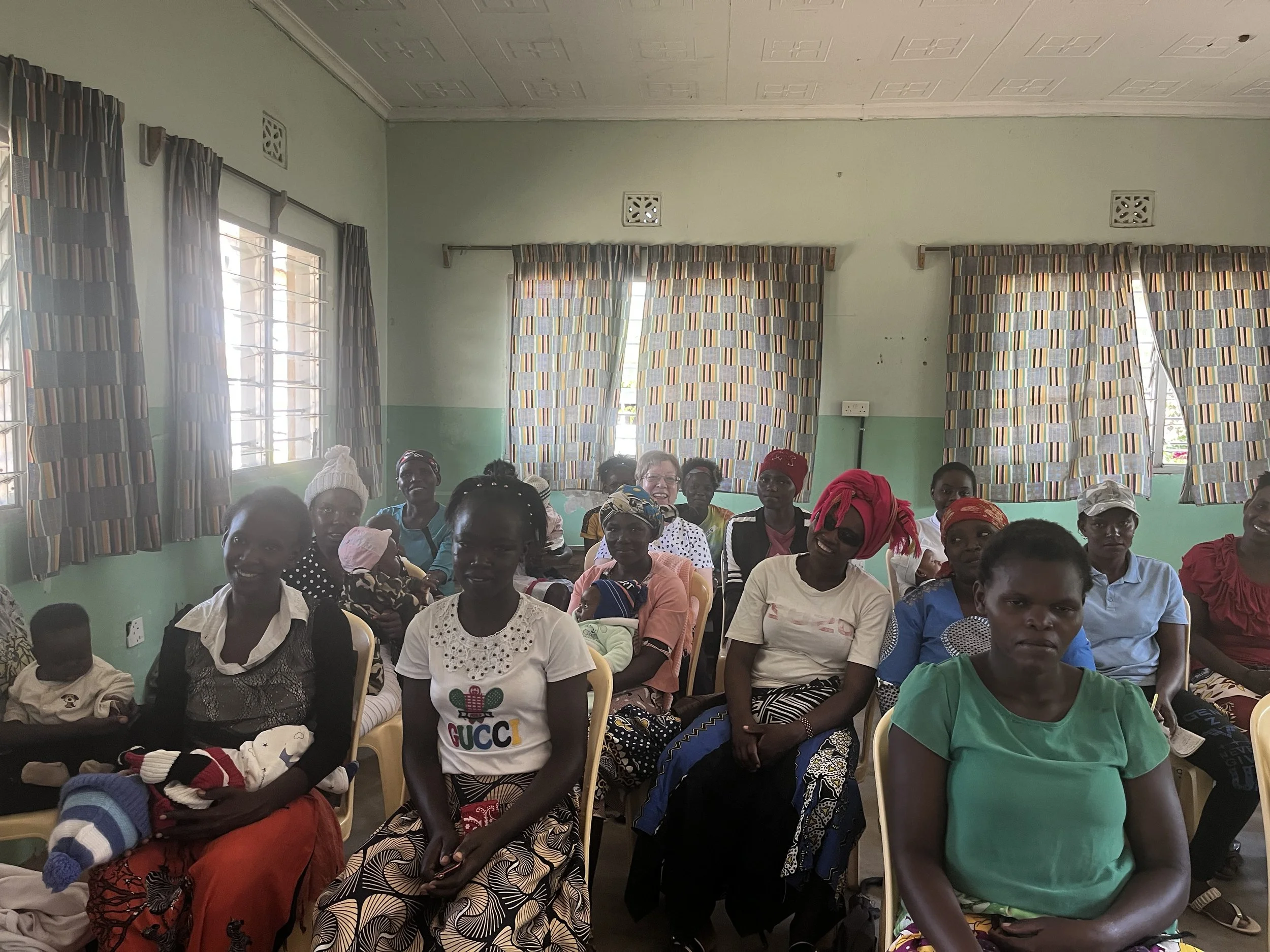 Group of women sitting on chairs in a room with patterned curtains and green walls.