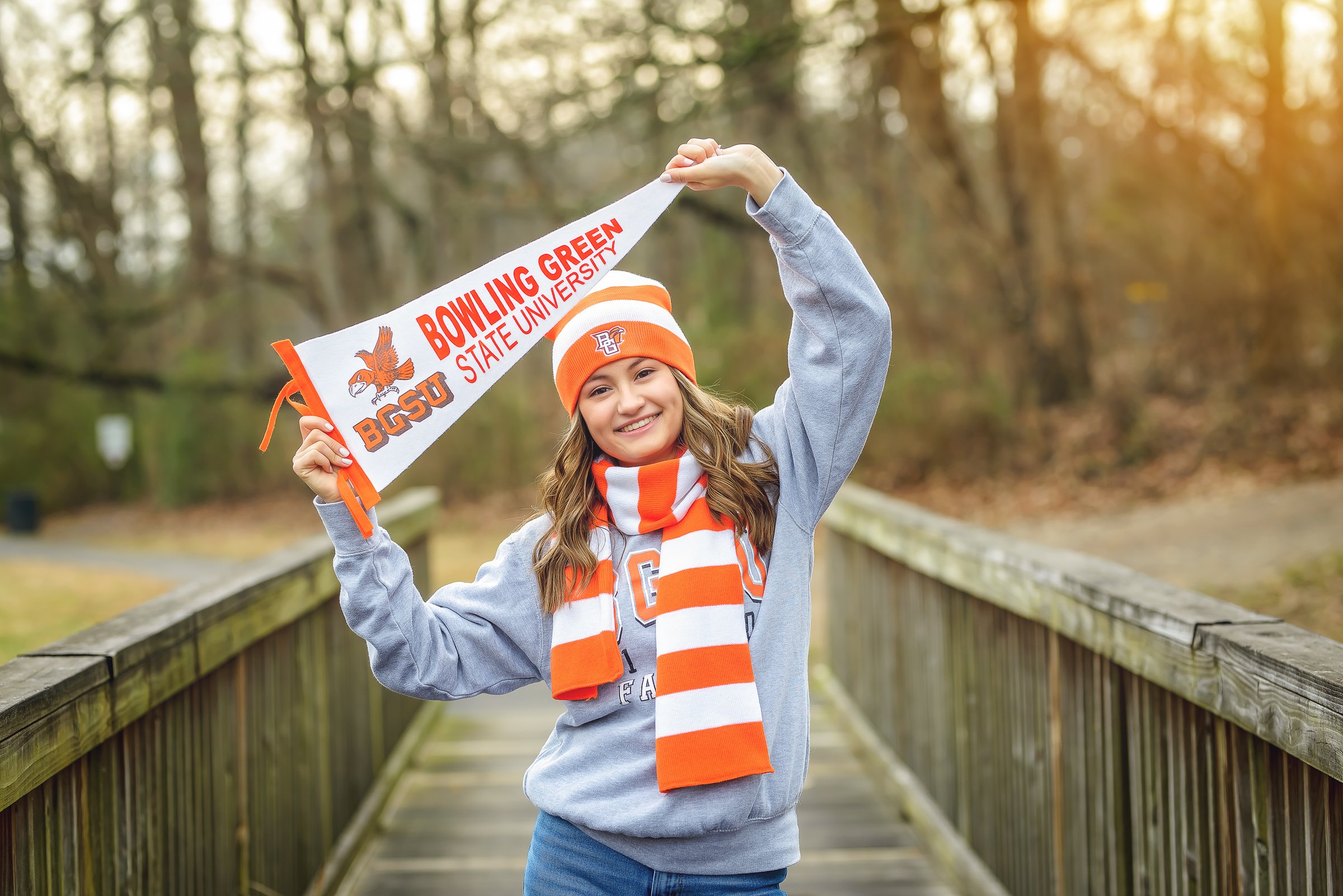 Senior girl celebrating her Bowling Green State University commitment while holding a pennant on a wooden bridge