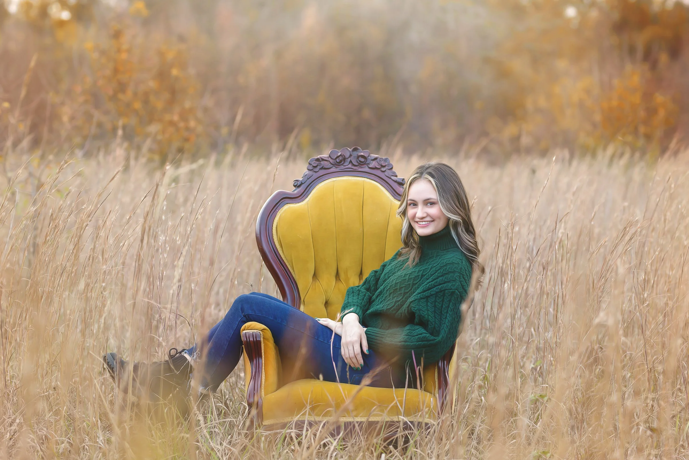 Senior girl sitting in a vintage yellow chair in a tall autumn field during her fall senior photo session in Charlotte, NC