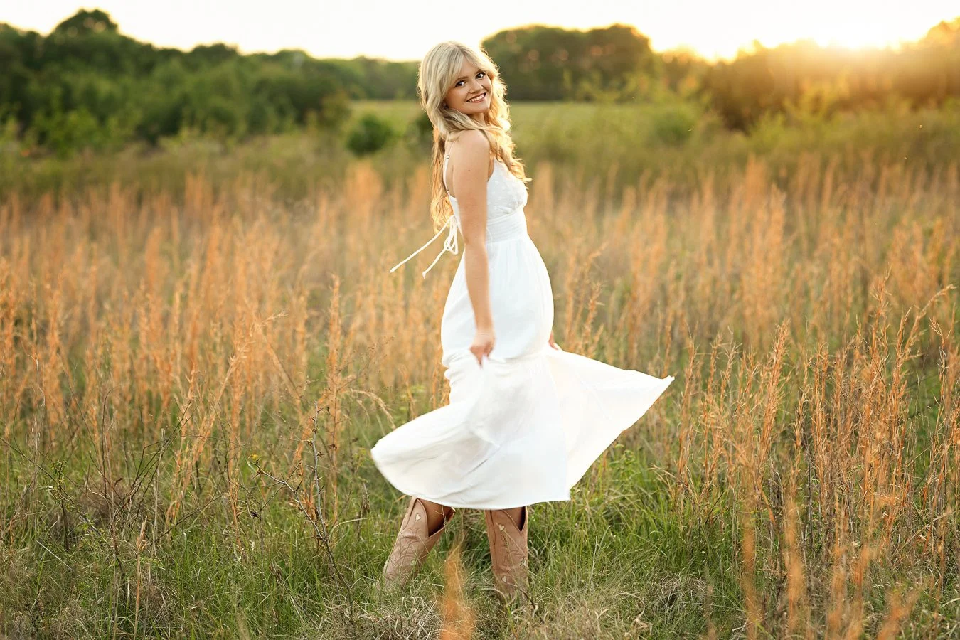 A smiling woman in a white dress twirling in a grassy field at sunset in Harrisburg NC