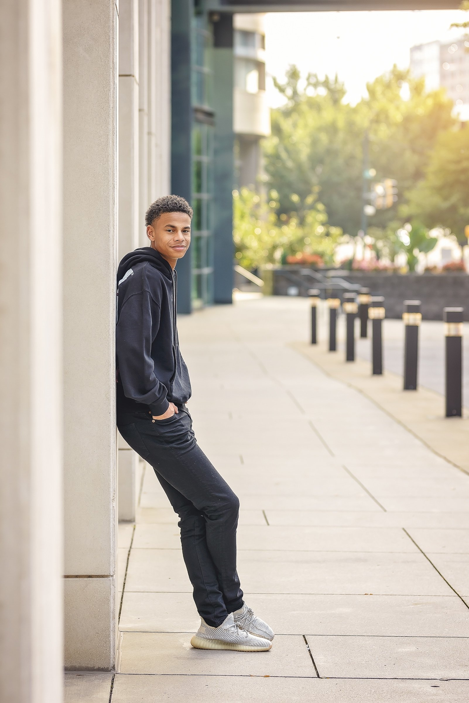 high school senior boy photographed in uptown charlotte in black hoodie and jeans modern editorial image