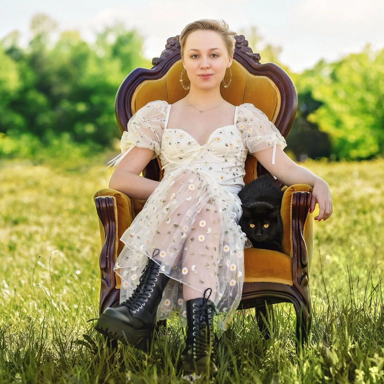 Senior girl sitting in a vintage velvet chair outdoors with a black cat beside her