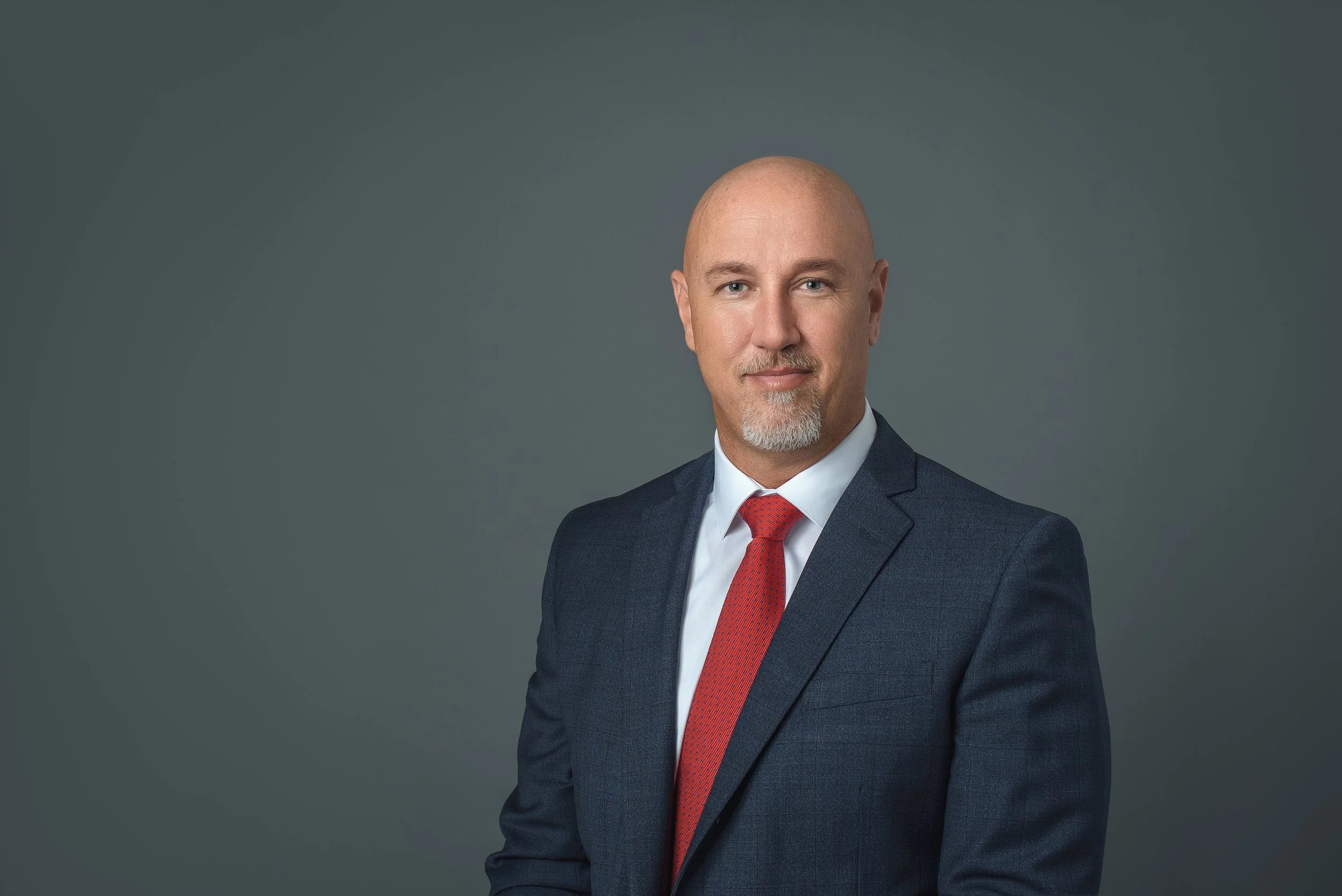 Professional business headshot of a man in a navy suit with a red tie on a gray studio background in Charlotte NC