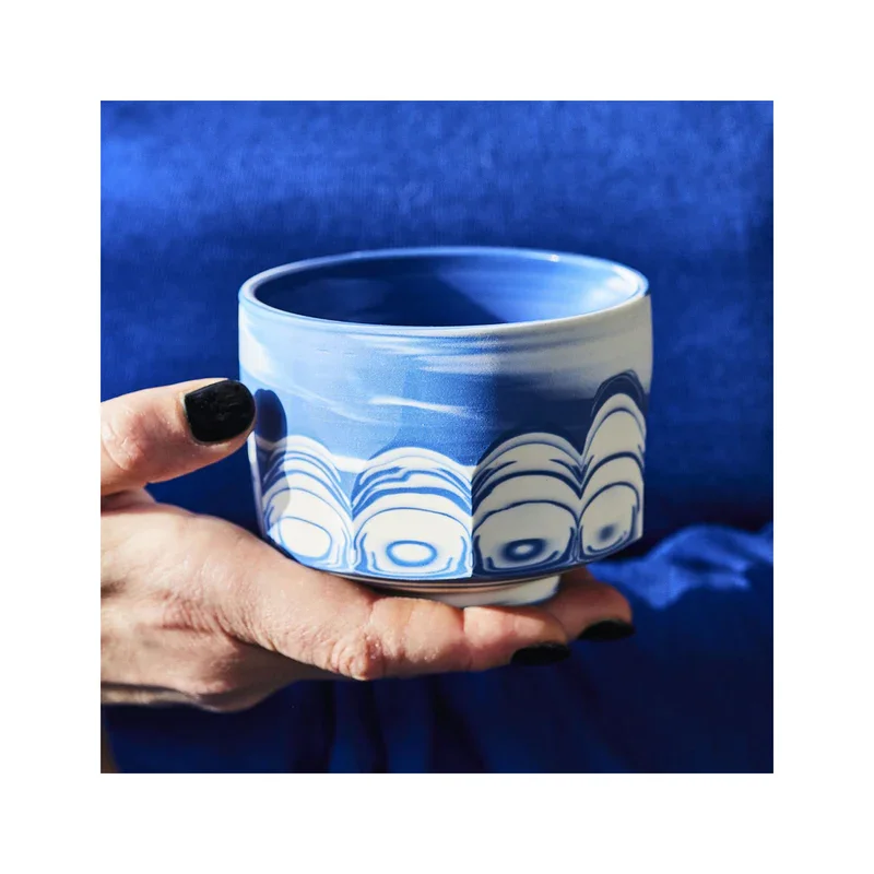 Hand hält eine kunstvolle, blau-weiße Keramikschale von Annika Schüler vor einem blauen Hintergrund.
