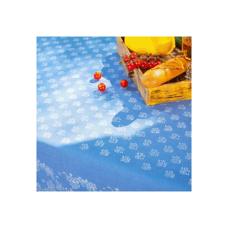 Blaue Tischdecke mit weißem, abgedruckten Muster von J.H. Koch Werkstätten. Darauf liegt ein Korb mit Baguette, Tomaten und Käse.