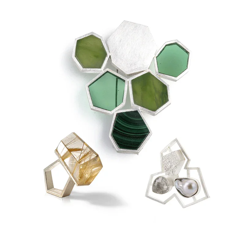Mehrere geometrische Schmuckstücke von Babette von Dohnanyi, darunter Anhänger mit grünen, weißen, goldenen, silbernen Steinen und Perlen, in verschiedenen Formen und Größen.