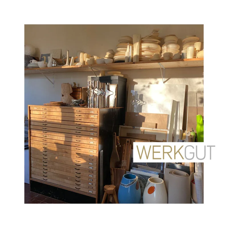 Holzregal mit vielen keramischen Geschirrstücken und Zubehör in einer Werkstatt, darauf das Logo "Werkgut"