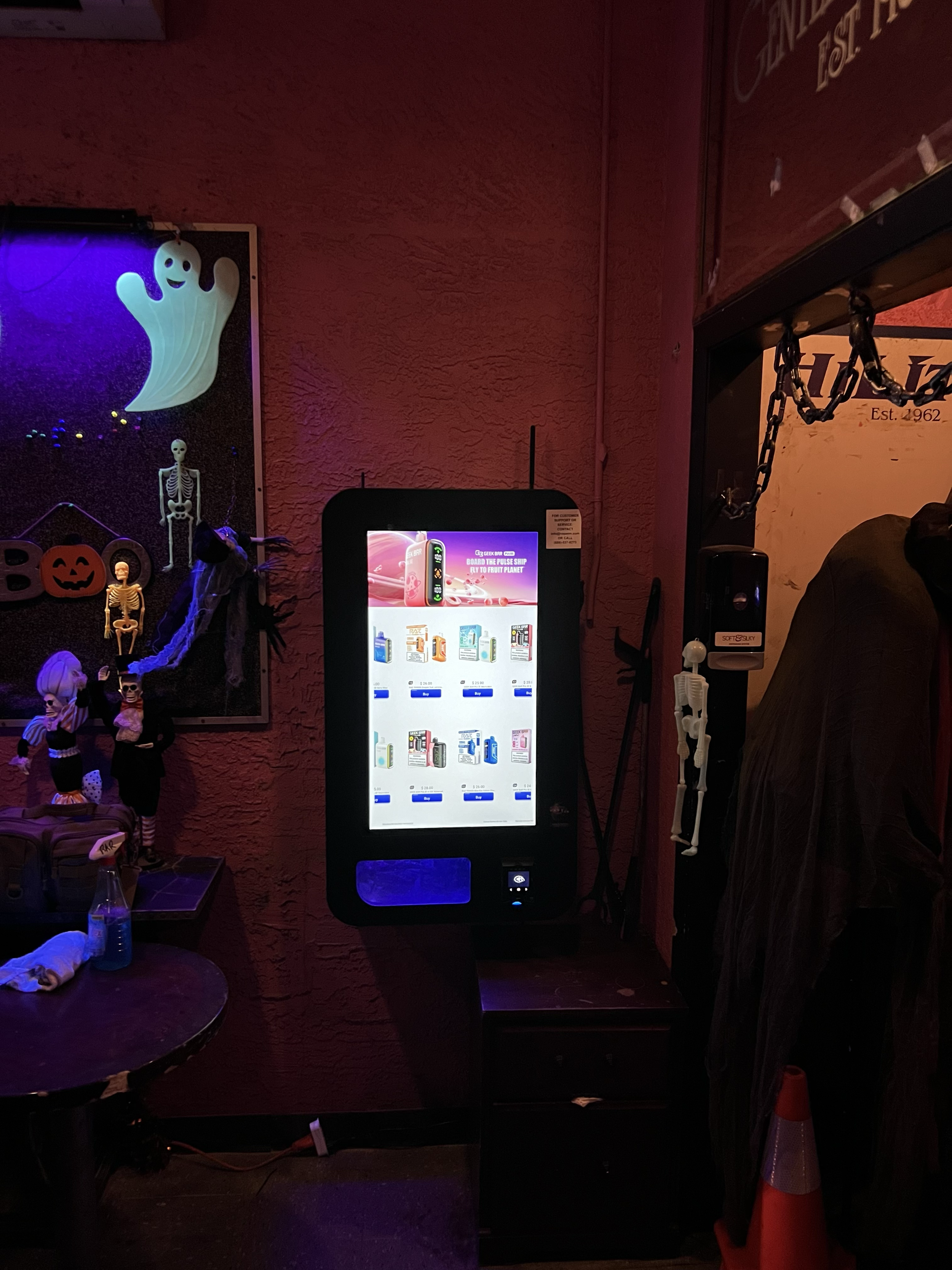 Vape vending machine installed in a dimly lit, Halloween-themed bar with skeleton décor, showcasing in-venue convenience for adult nightlife patrons.