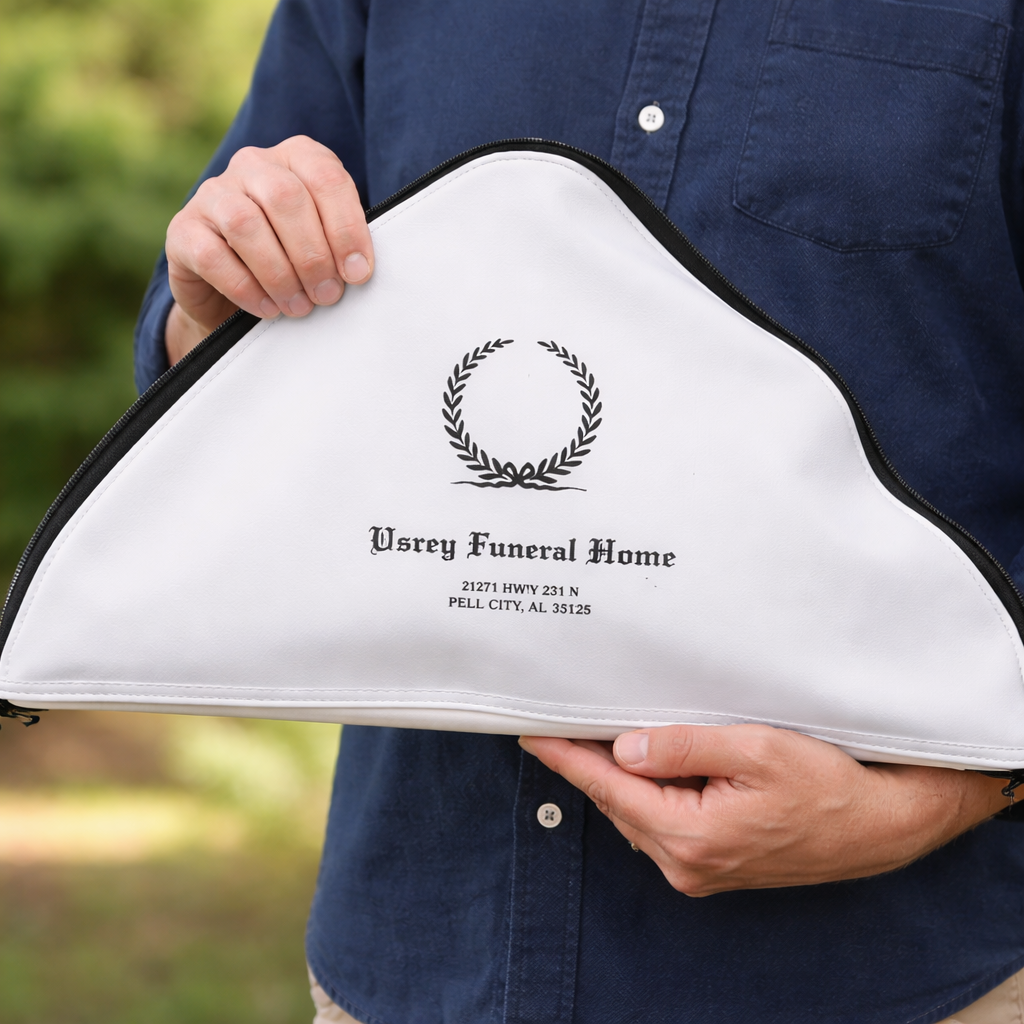 Person holding a white funeral home casket with the words 'Usrey Funeral Home' and an address, featuring a black laurel wreath logo, outdoors.