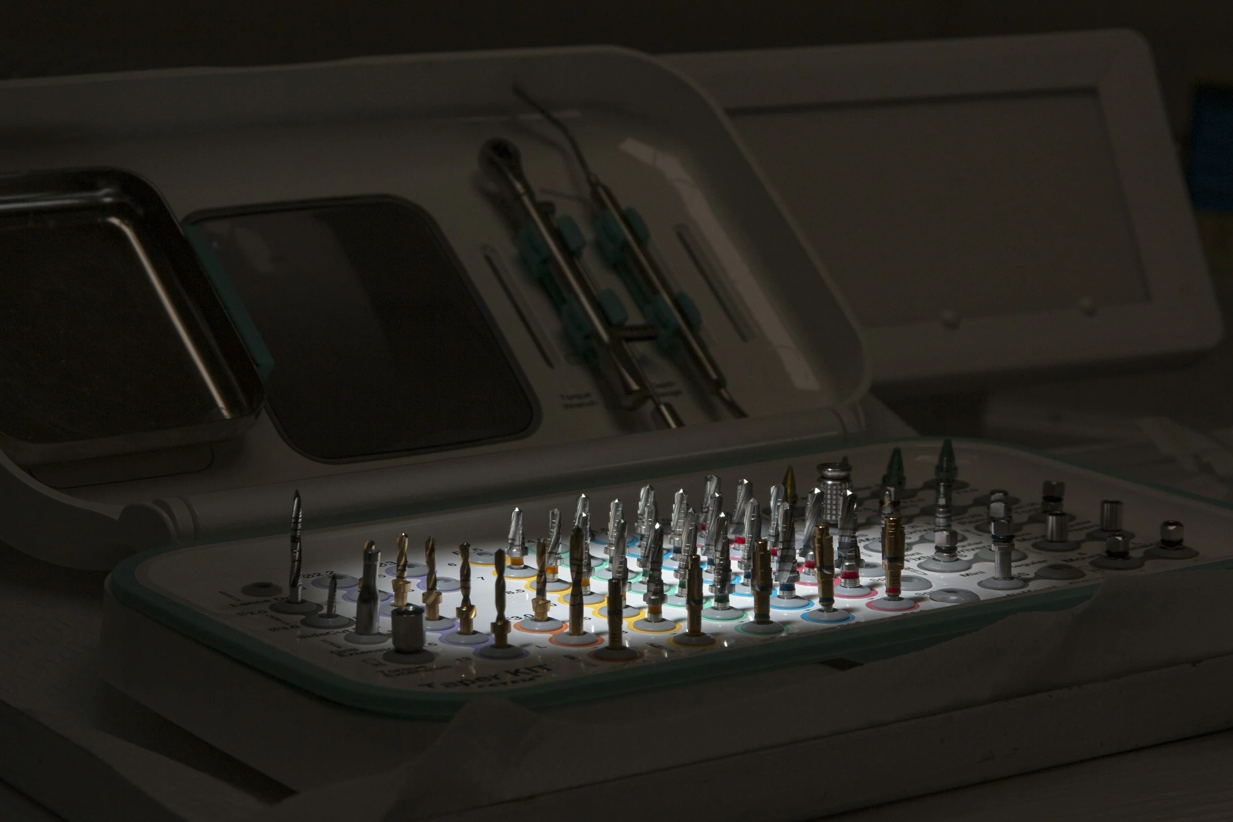 Dental surgical toolkit with various dental burs and tools, dimly lit with some illuminated instruments.