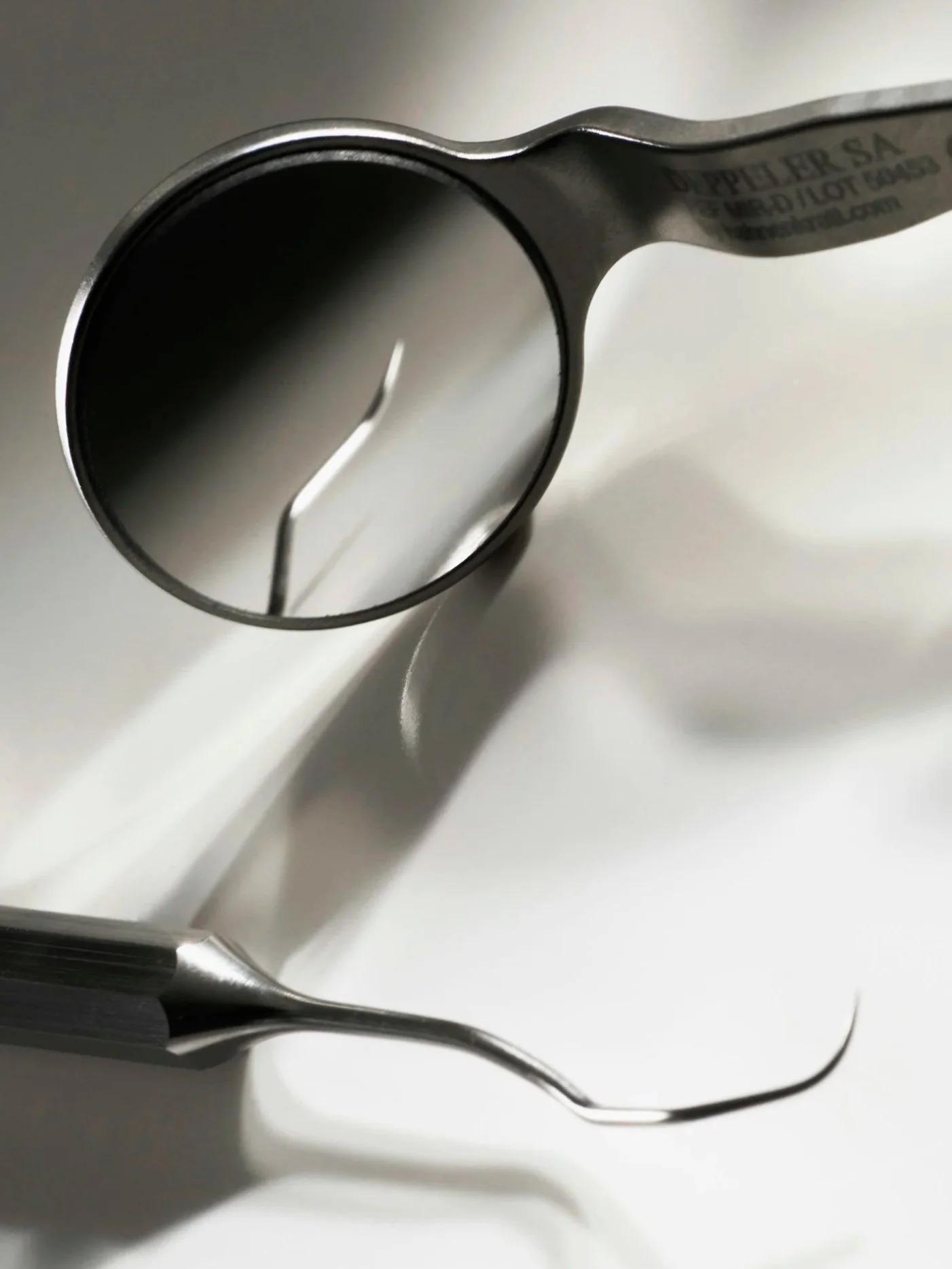 Close-up of dental tools, including a dental mirror and a probe, on a white surface.