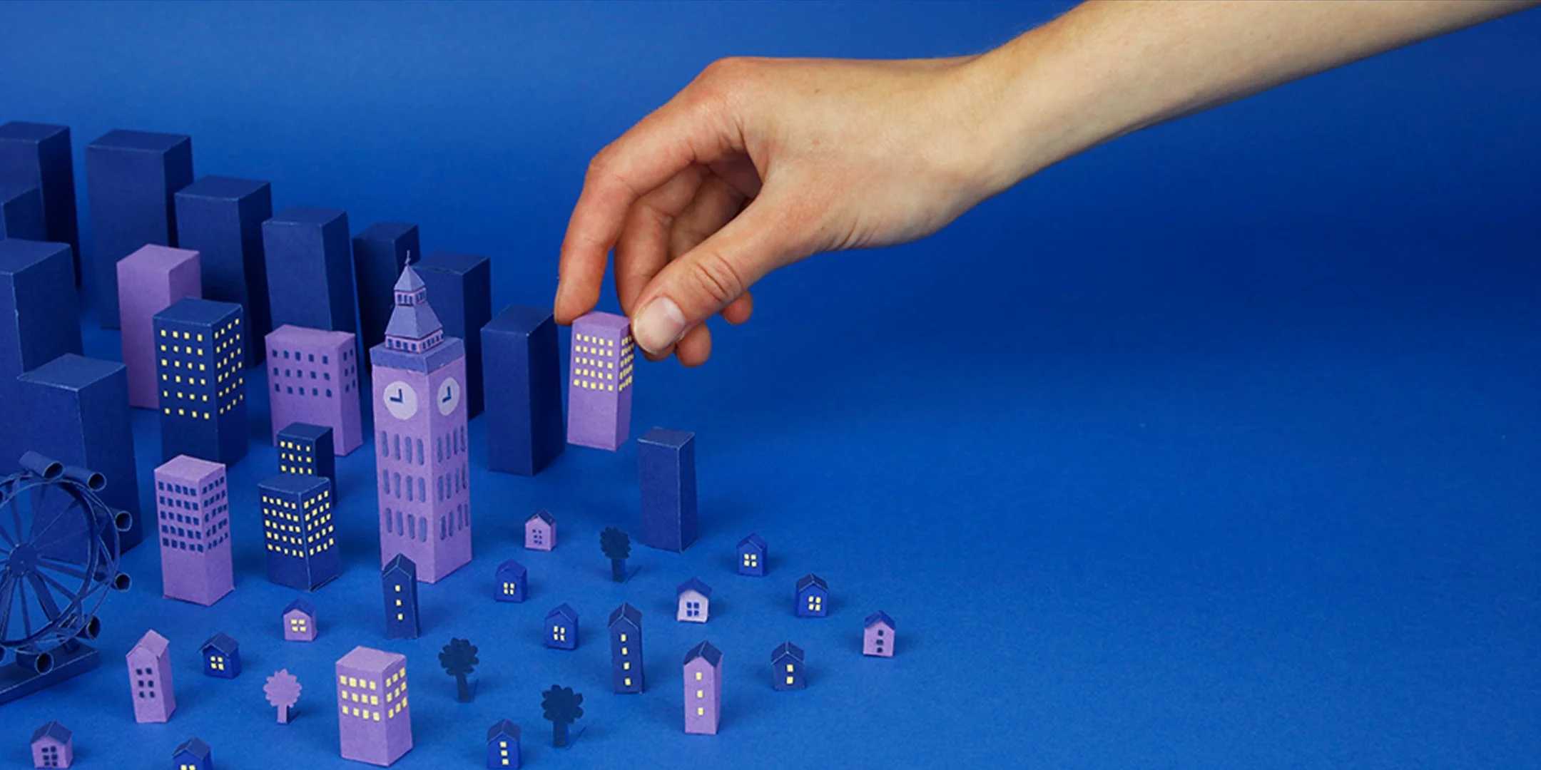 Props made of paper. Buildings and London landmarks made of paper. A hand is reaching in to pick up a skyscraper. 