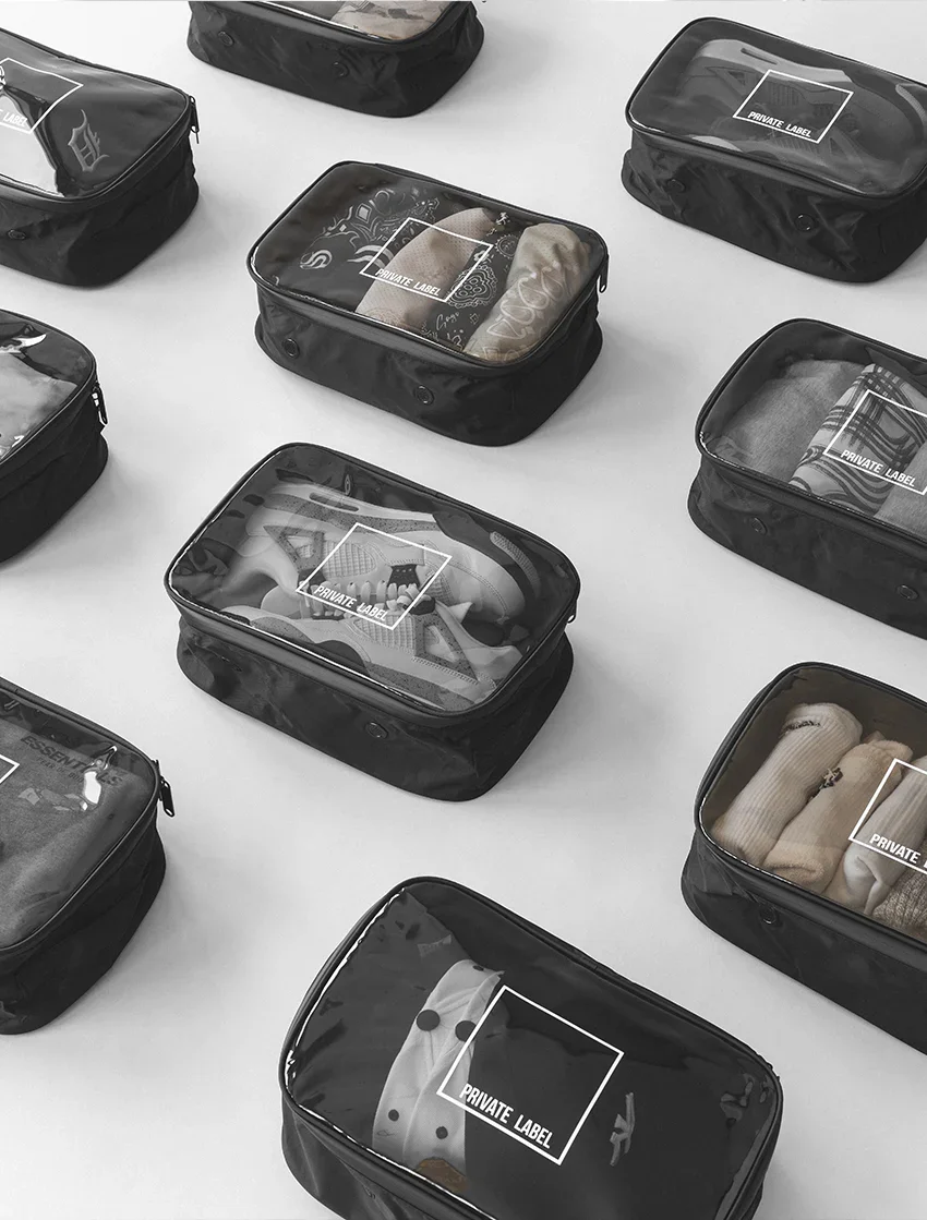 Multiple black travel pouches with transparent tops labeled "Private Label" displaying various clothes and accessories inside, arranged on a white surface.