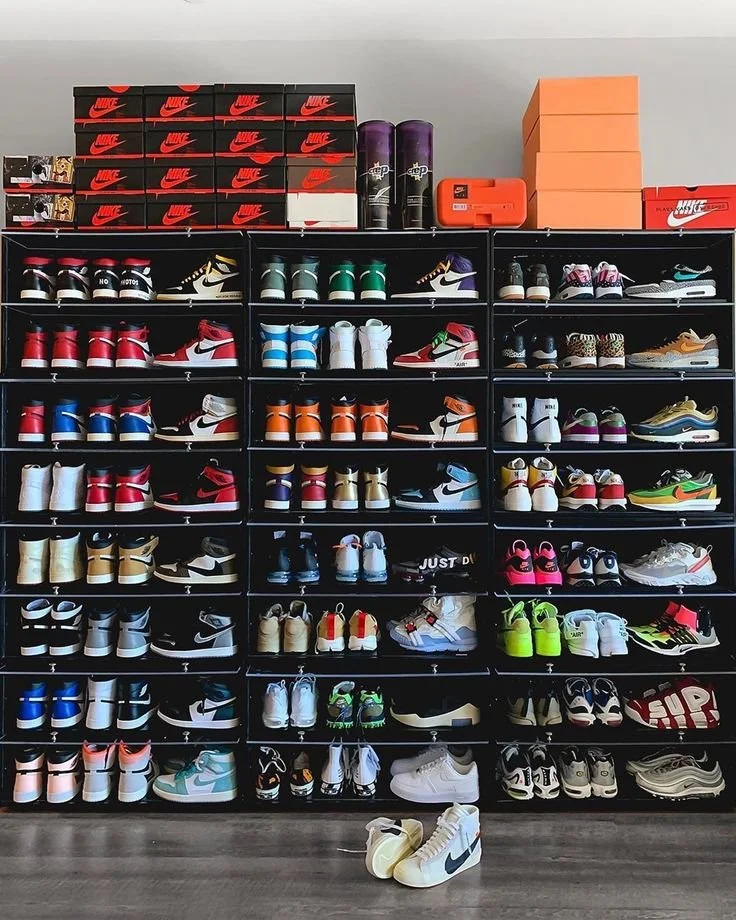 A large black shoe rack filled with colorful Nike sneakers, with Nike shoeboxes stacked on top and a pair of sneakers on the floor in front.