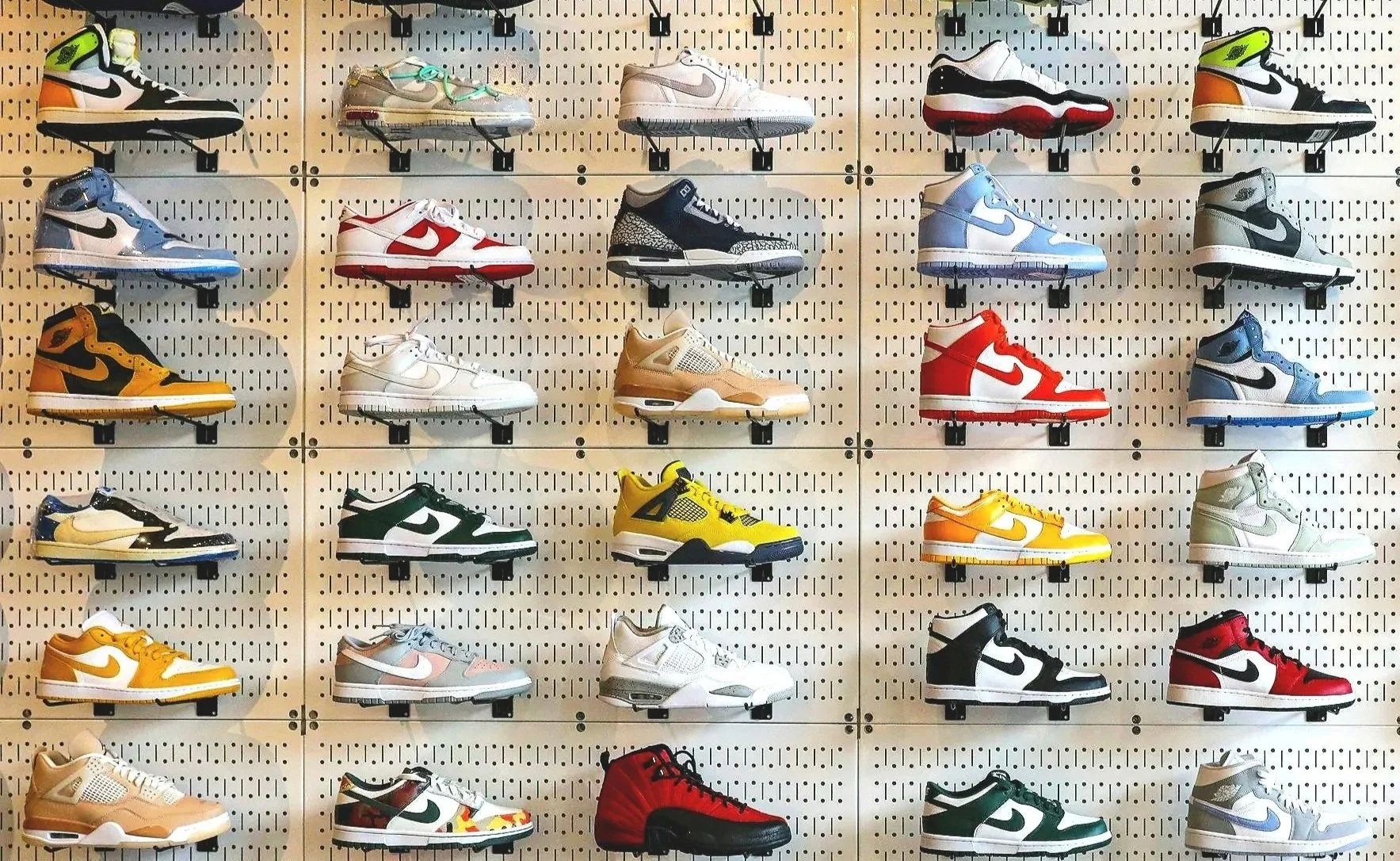 A sneaker storage room with shelves filled with various sneakers, a red Supreme chair, and a mat on the floor that says 'KEEP OFF!'. There is a Jordan logo on the wall above the shelves.