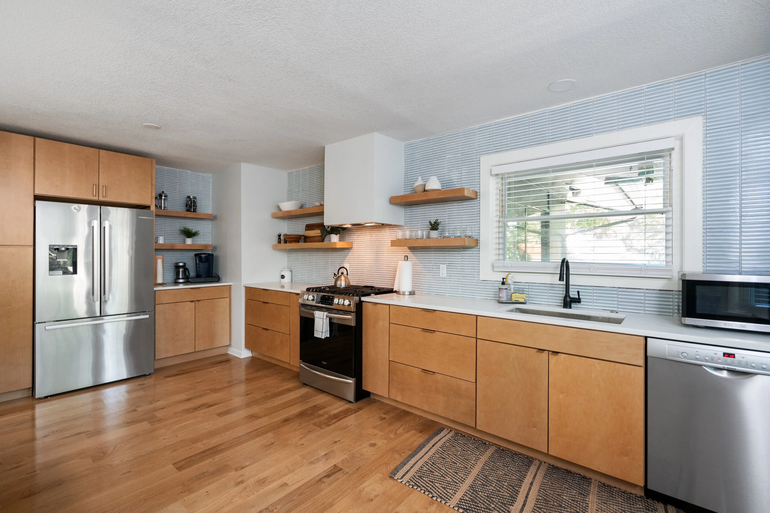 Modern kitchen with wooden cabinets, stainless steel refrigerator, microwave, and a window above the sink.