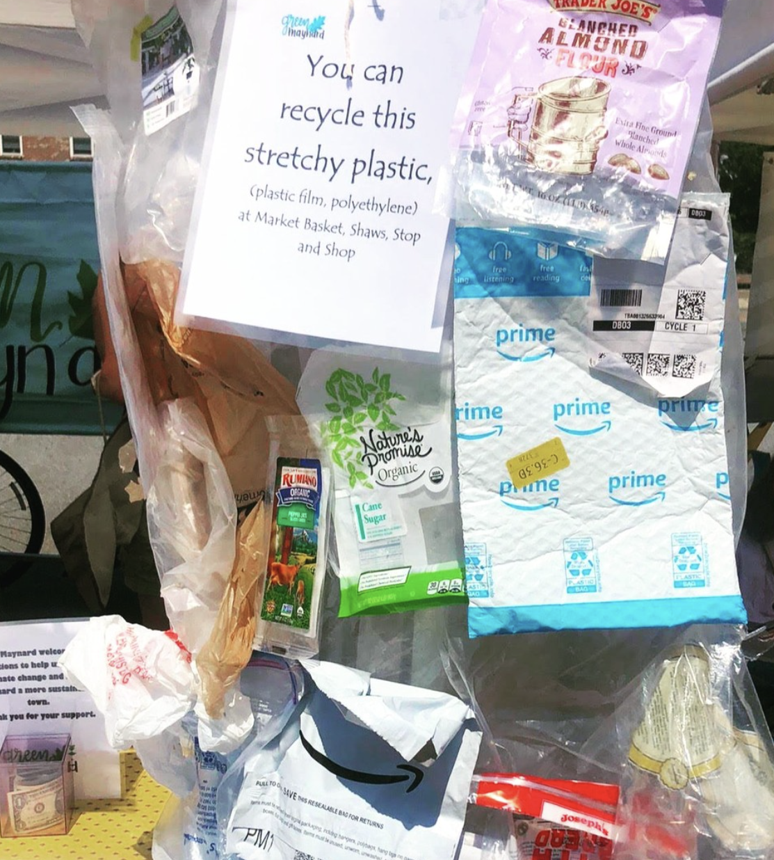 A collection of trash and recycling items, including a plastic bag with a sign encouraging recycling, a package of almond flour, a juice box, a paper bag from Amazon, and other miscellaneous packaging materials.