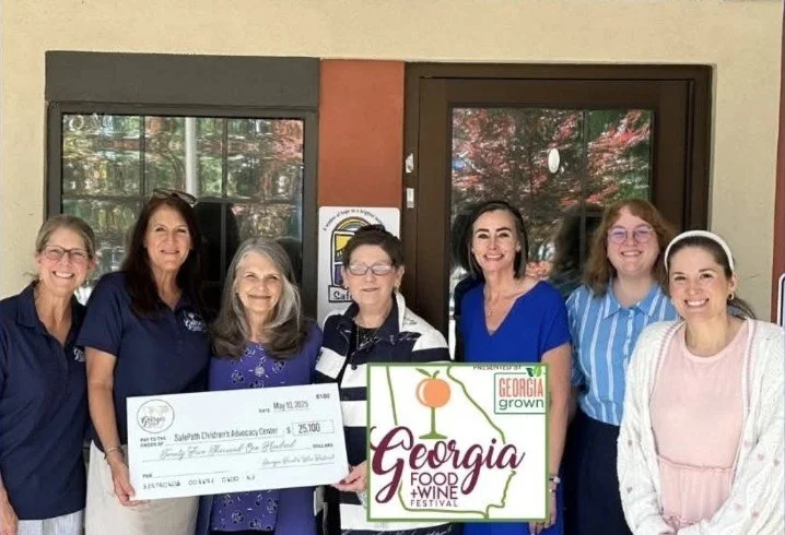 Seven women standing together outdoors, holding a large check and a Georgia Food & Wine Festival sign.