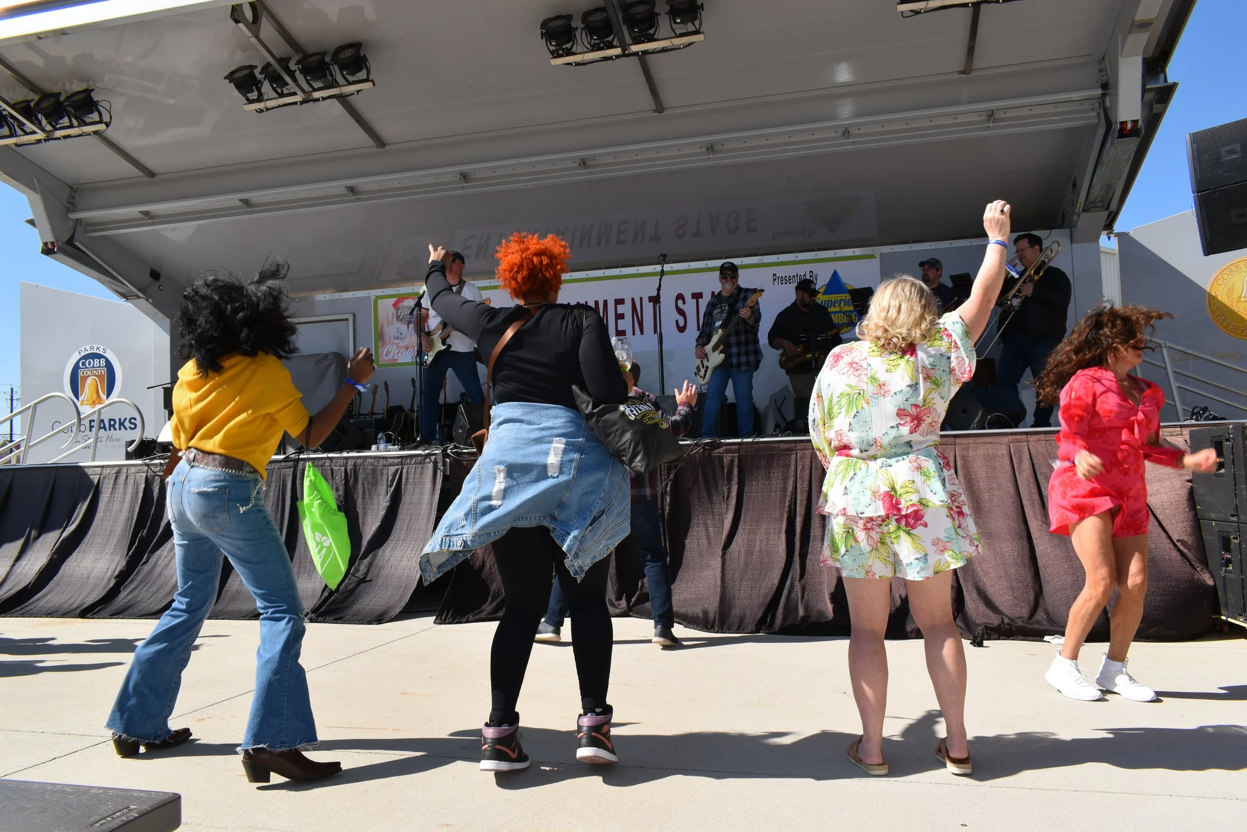People dancing in front of a live band performing on stage at an outdoor event.