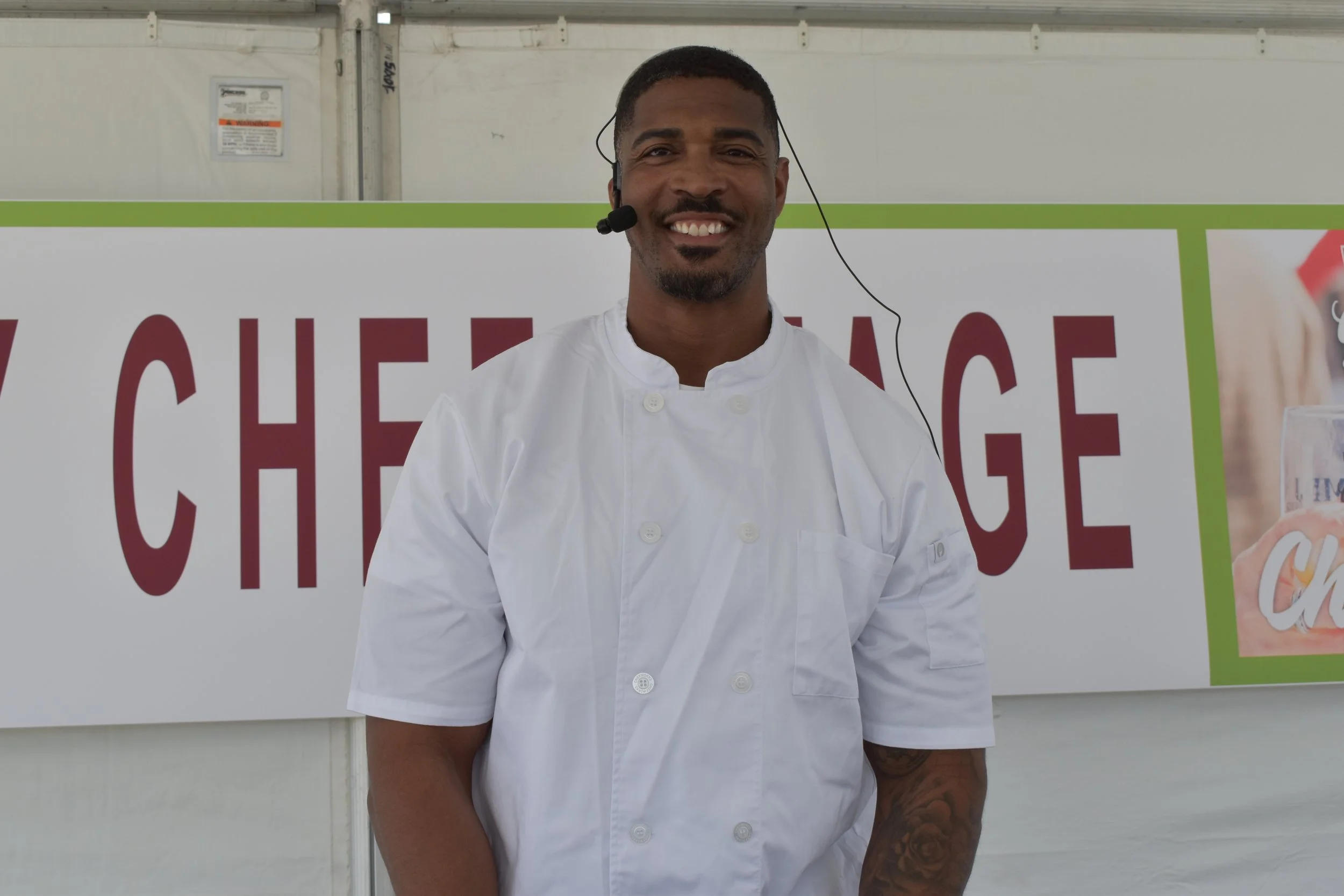 Man in a white chef's coat with a headset smiling in front of a large sign with the word 'CHALLENGE'.