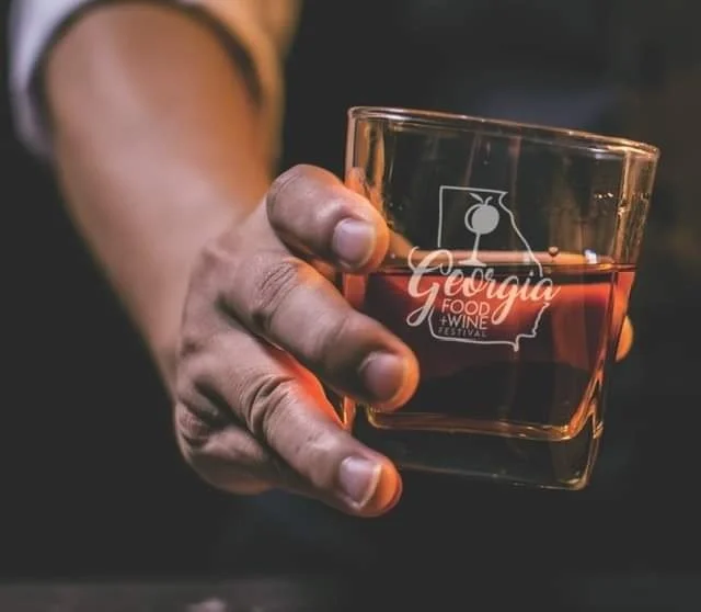 Person holding a glass of red wine with a Georgia Food & Wine Festival logo.