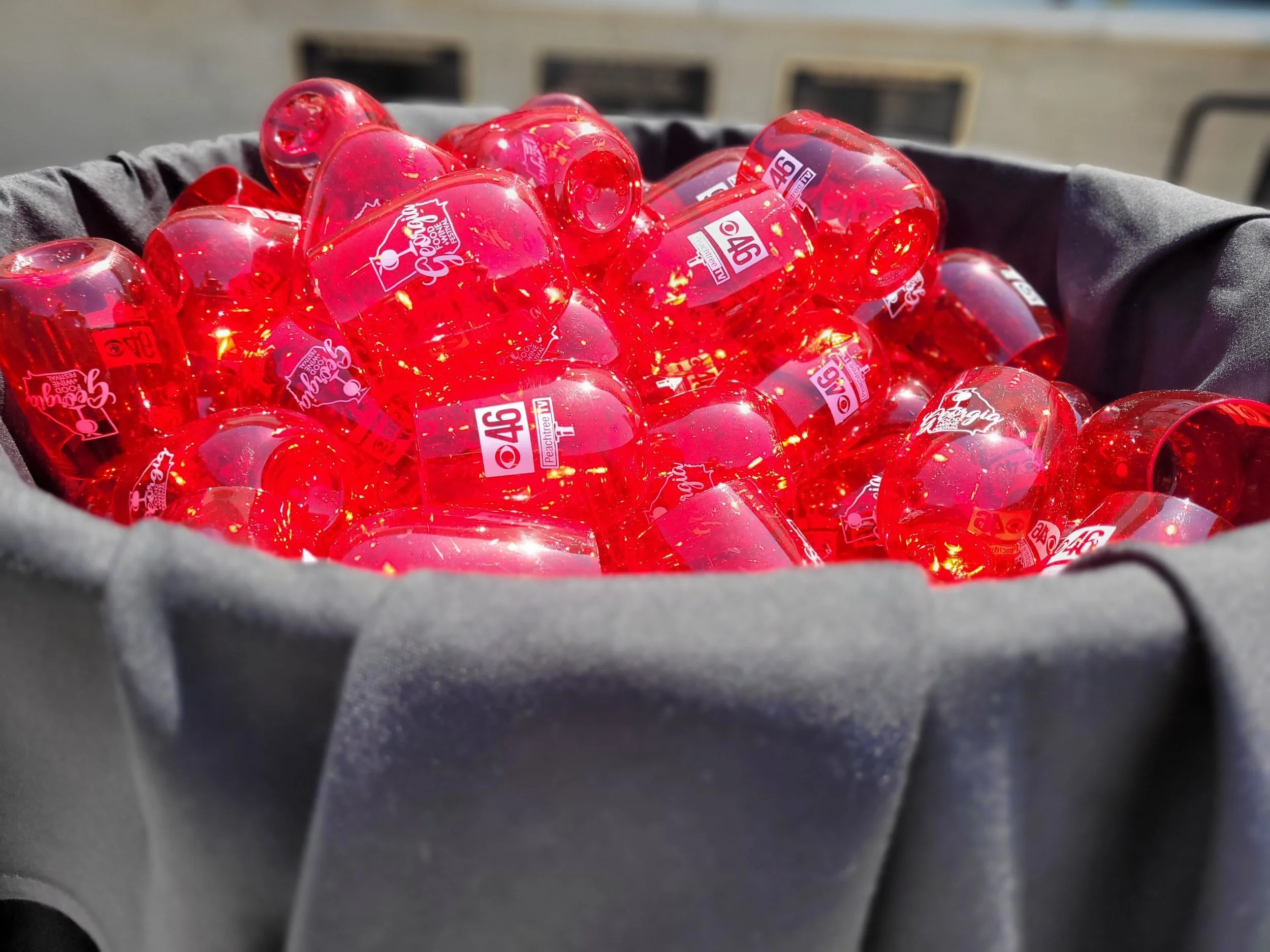 A black container filled with numerous red LEGO-shaped plastic cups with white and black logos and text on them.