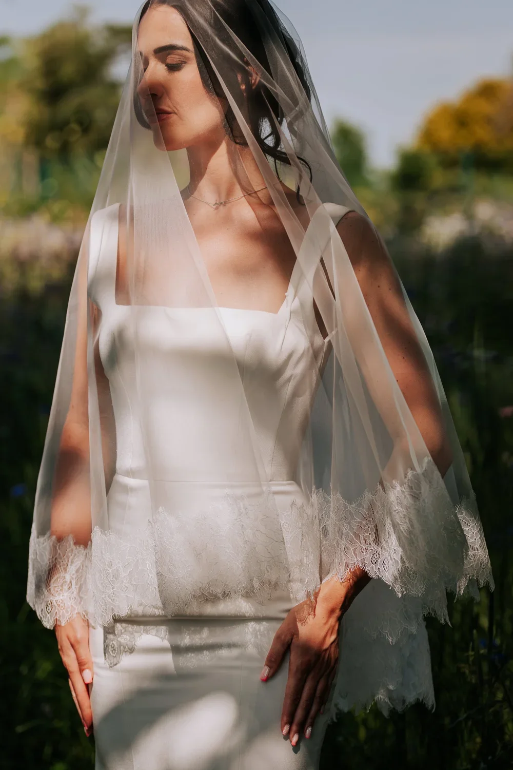 A bride wearing s couture gown with laced edge veil in a natural, open setting.