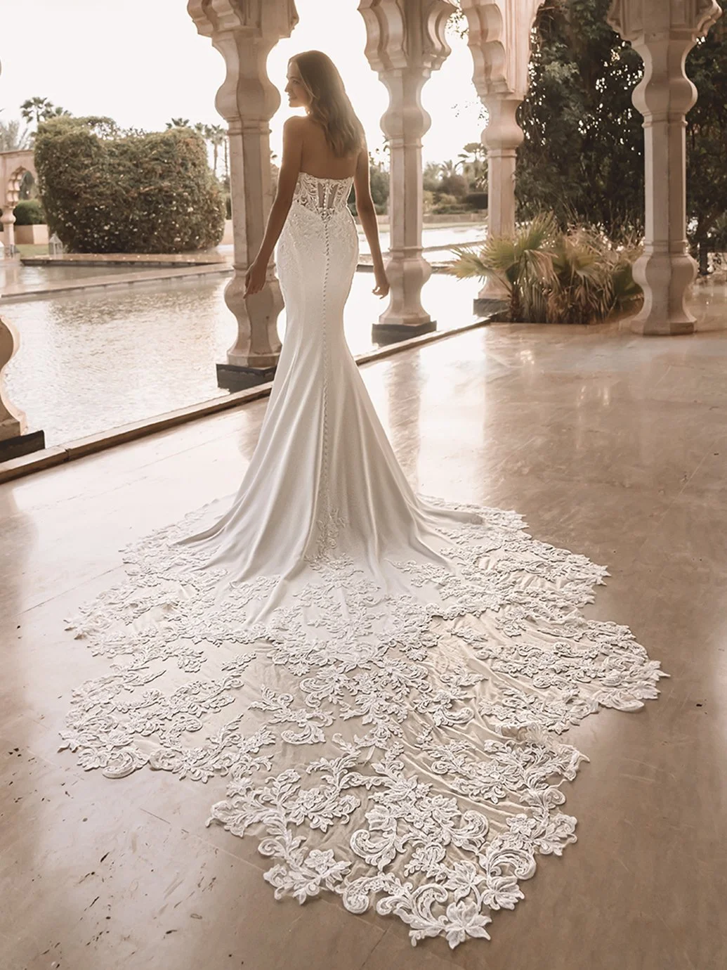 A bride in a lace couture gown with an extended train in an elegant architectural setting.