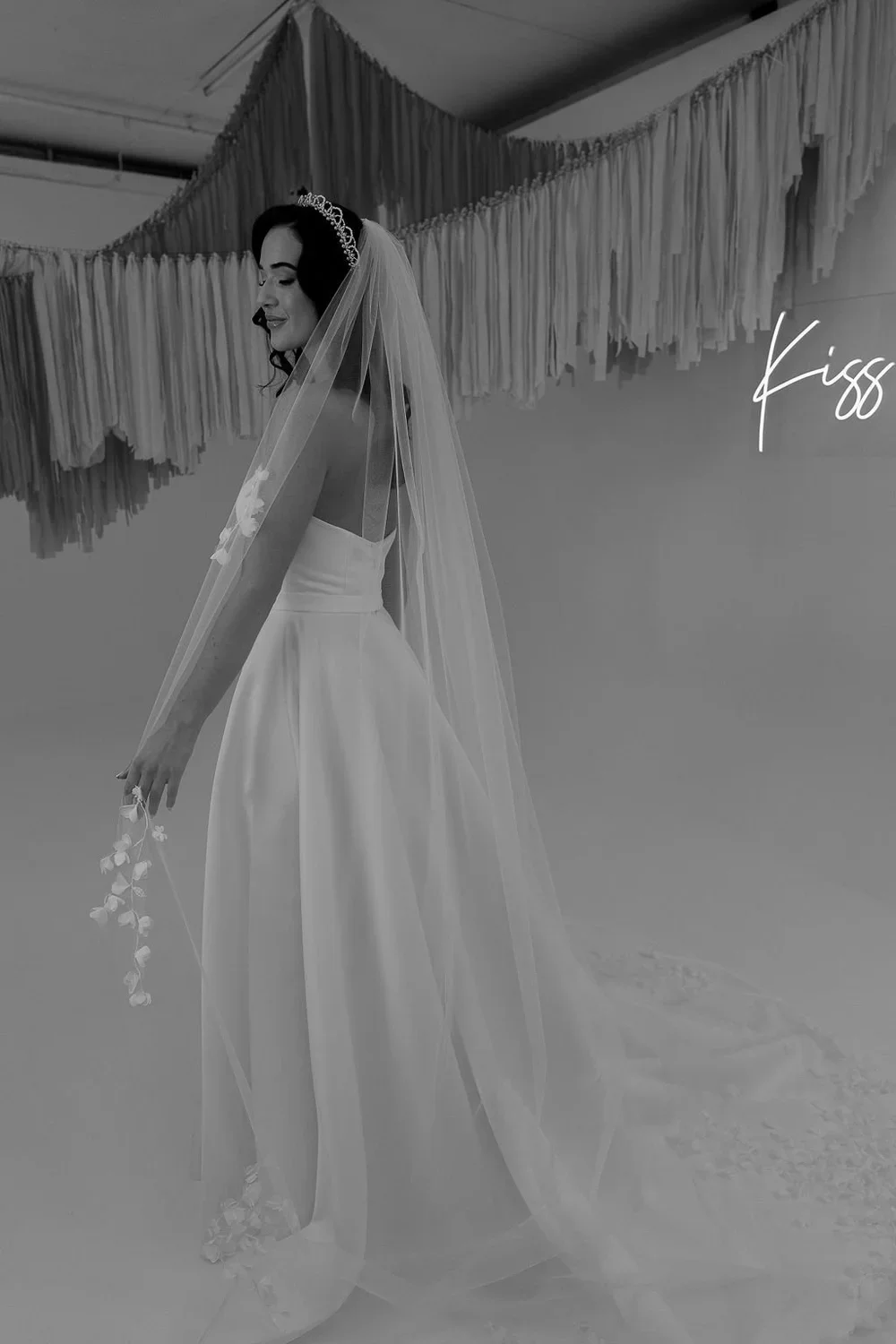 A bride in a sleeveless couture gown with veil and bouquet in an intimate interior setting.