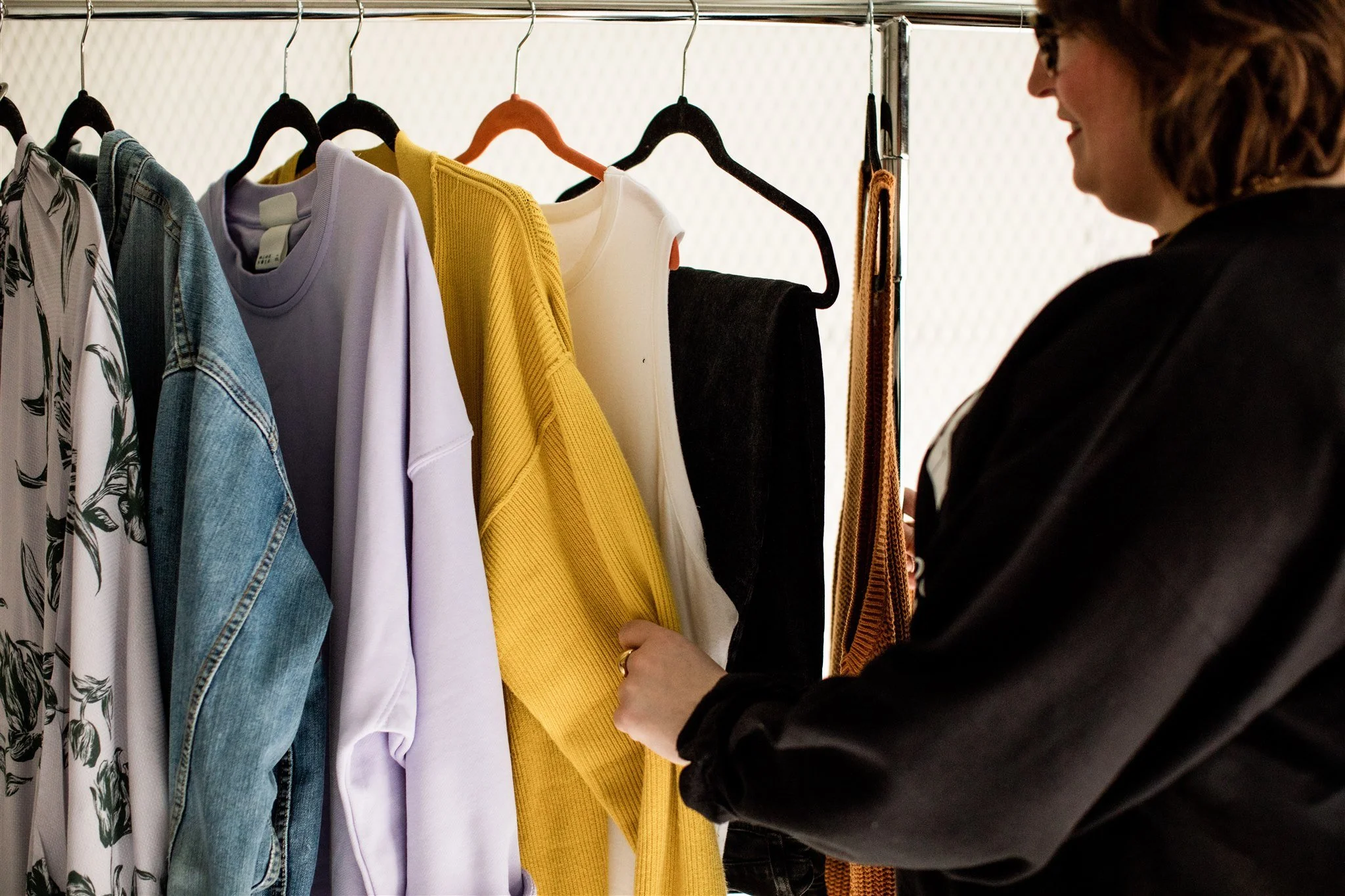 Person shopping for clothes, looking at a rack with various colorful shirts and jackets.