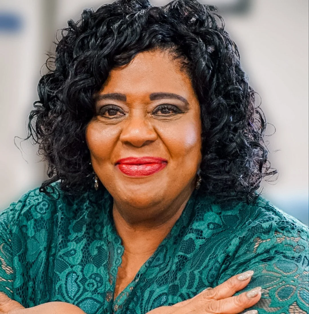 A woman with dark brown skin, curly black hair, and red lipstick smiling in a close-up portrait.